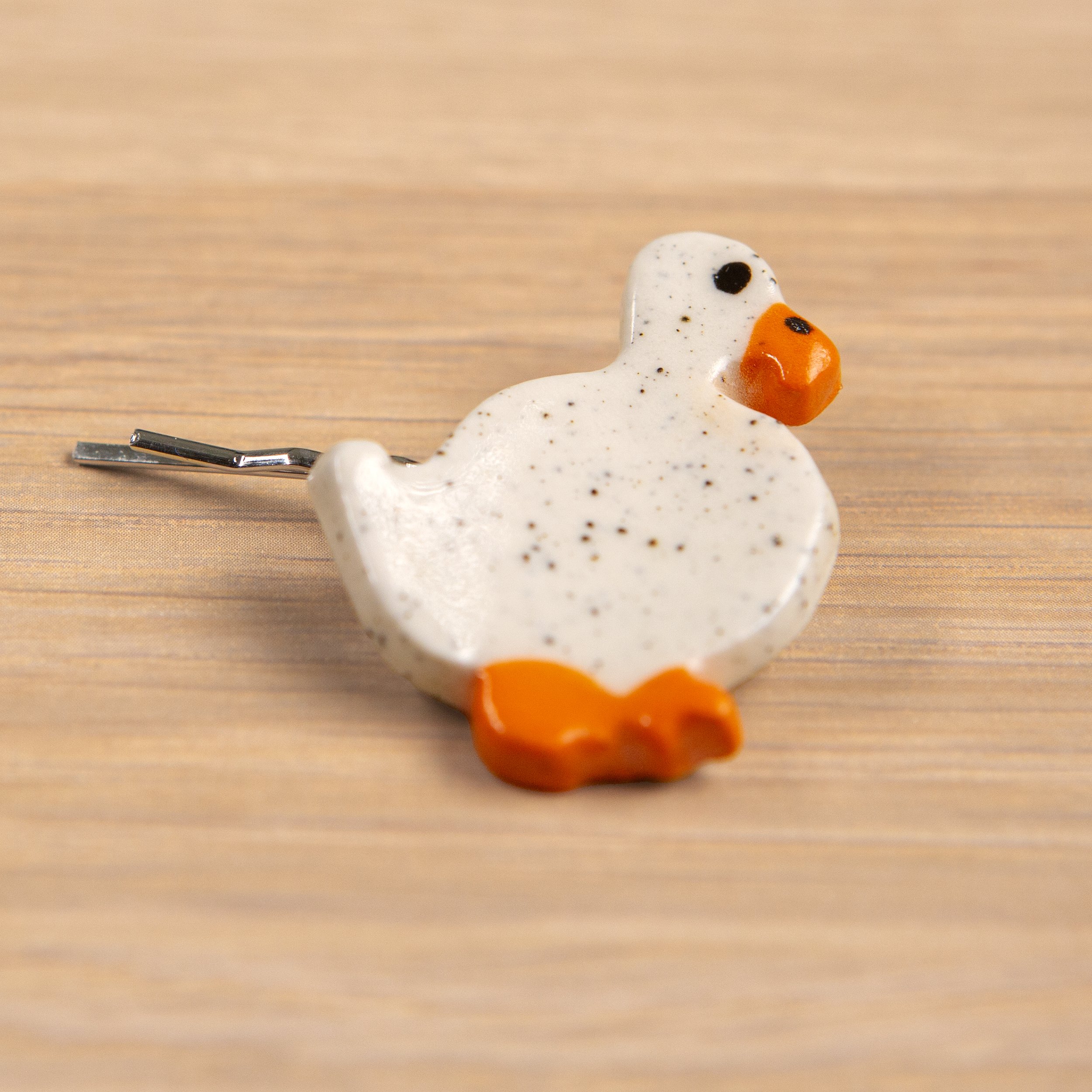 Handmade ceramic hair pin with a glossy wandering white duck, photographed on a neutral background.