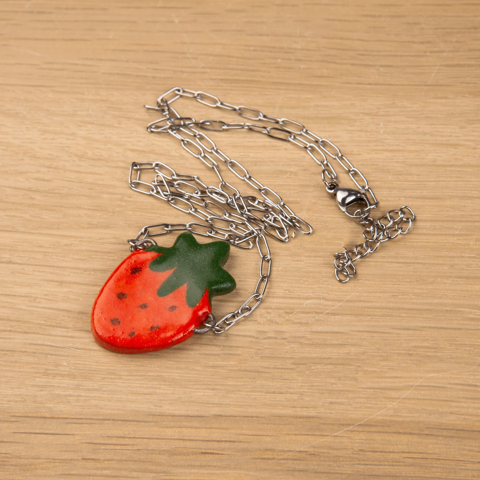 Handmade ceramic red strawberry necklace featuring a playful hand-painted strawberry pendant on a silver-coloured chain.