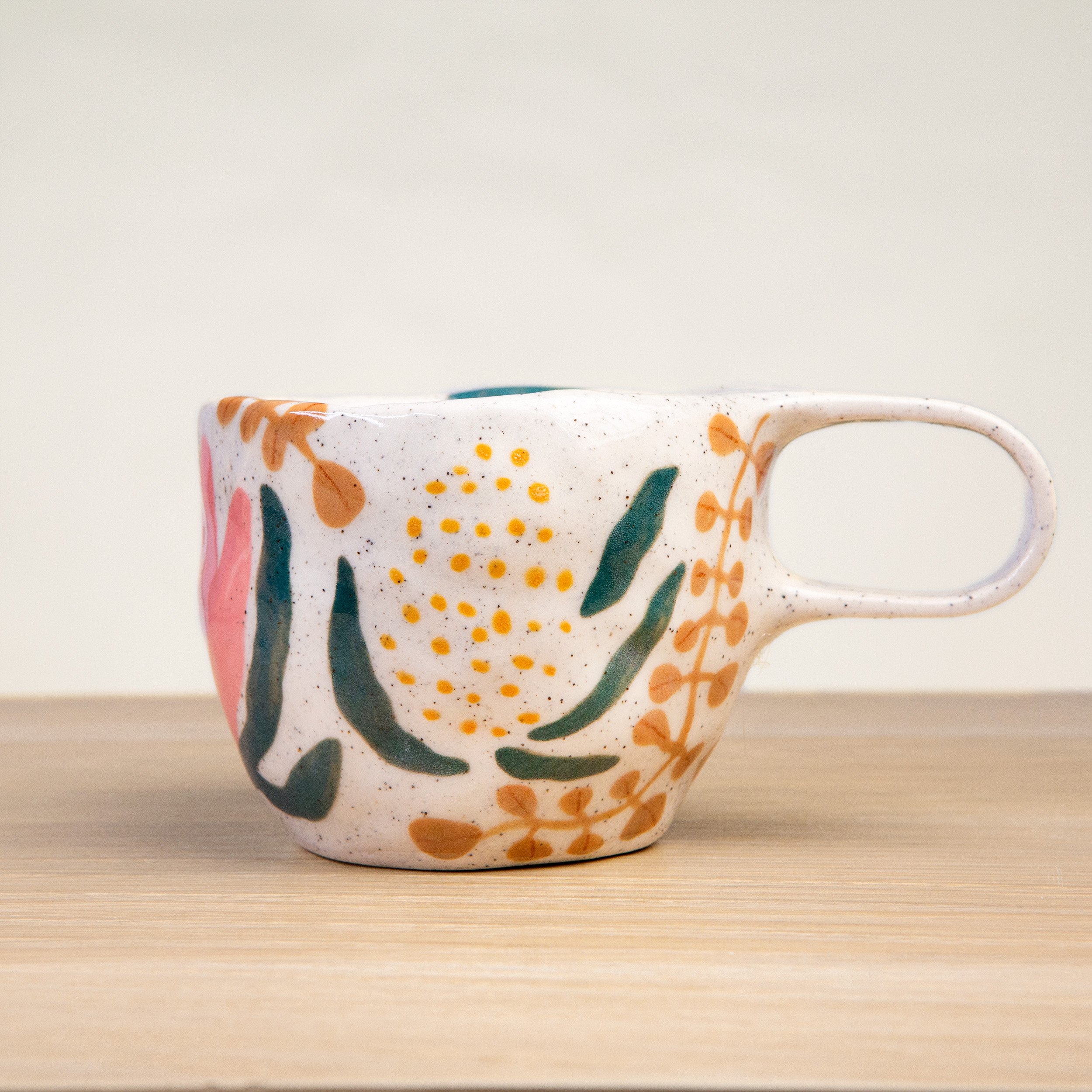 Handmade ceramic coffee cup with hand-painted native flowers, crafted from speckled clay in Melbourne. Holds approximately 150ml.