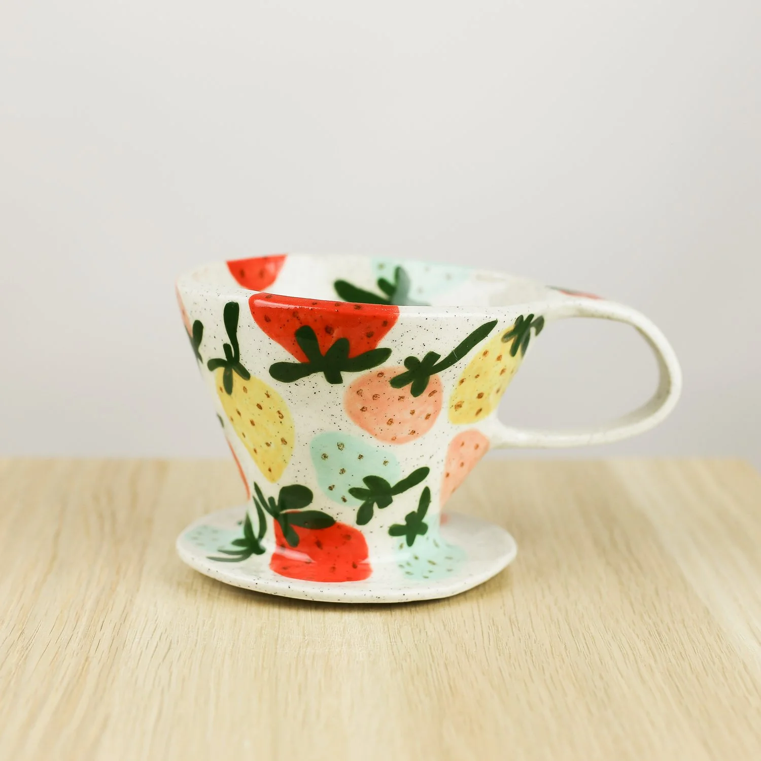 Handmade ceramic strawberry coffee dripper placed on a strawberry check cup, styled together on a soft, light background