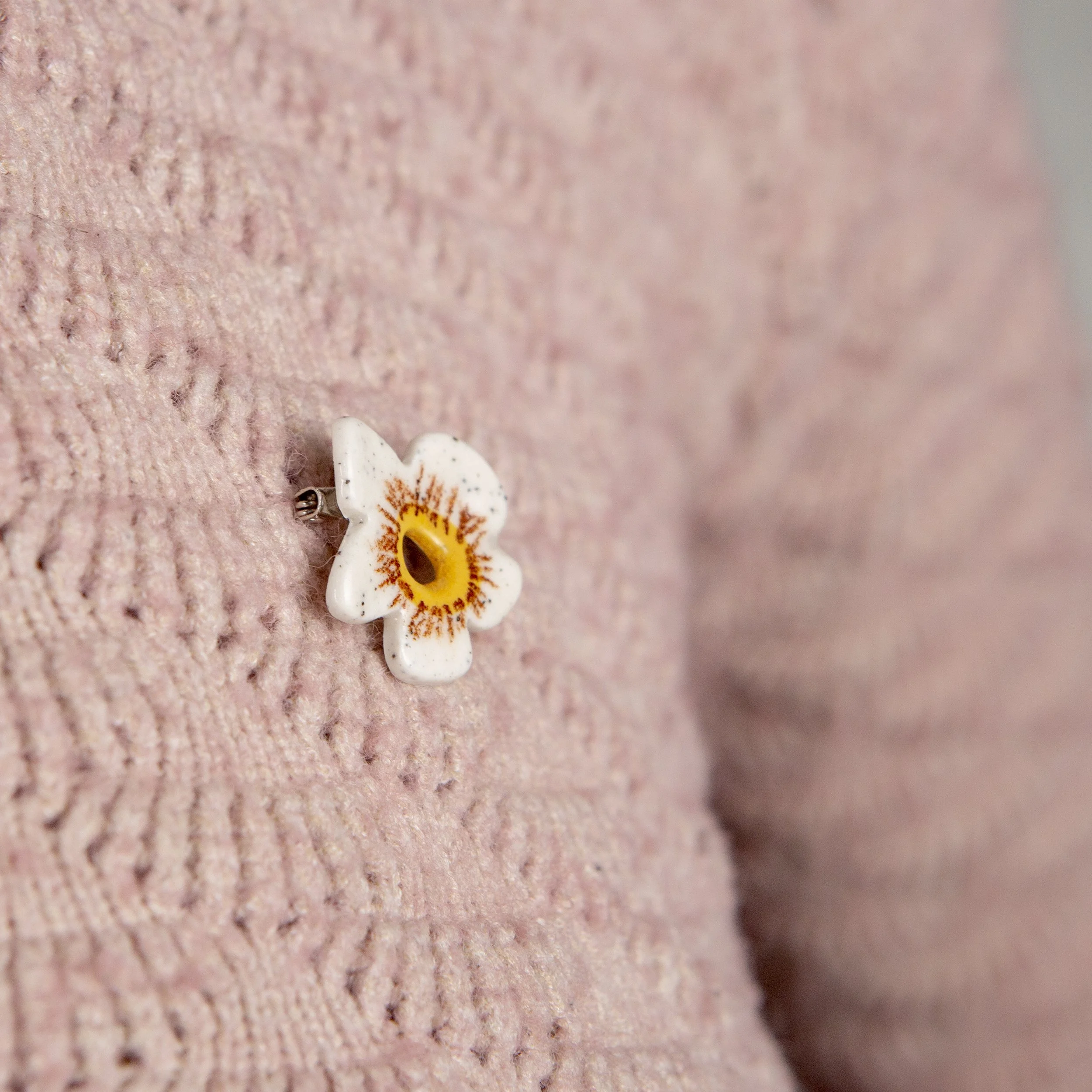 Handmade ceramic brooch with a glossy white flower, photographed on a neutral background