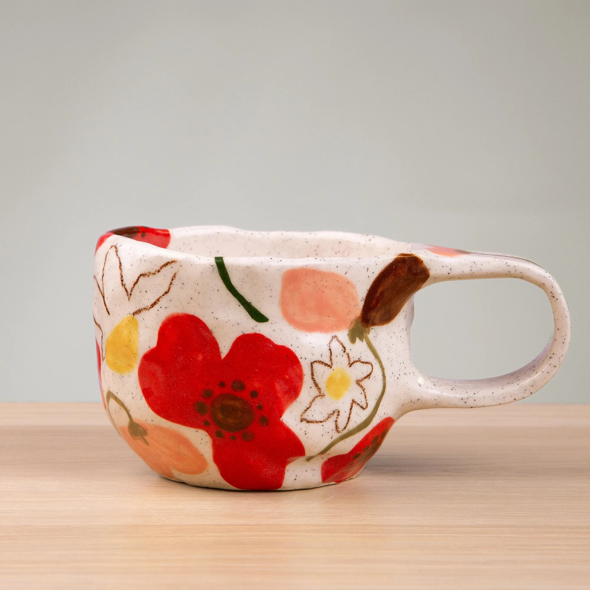 A soft garden in bloom, this handmade ceramic mug is adorned with hand-painted poppies, daisies and sweet pea flowers in a delicate, painterly style.