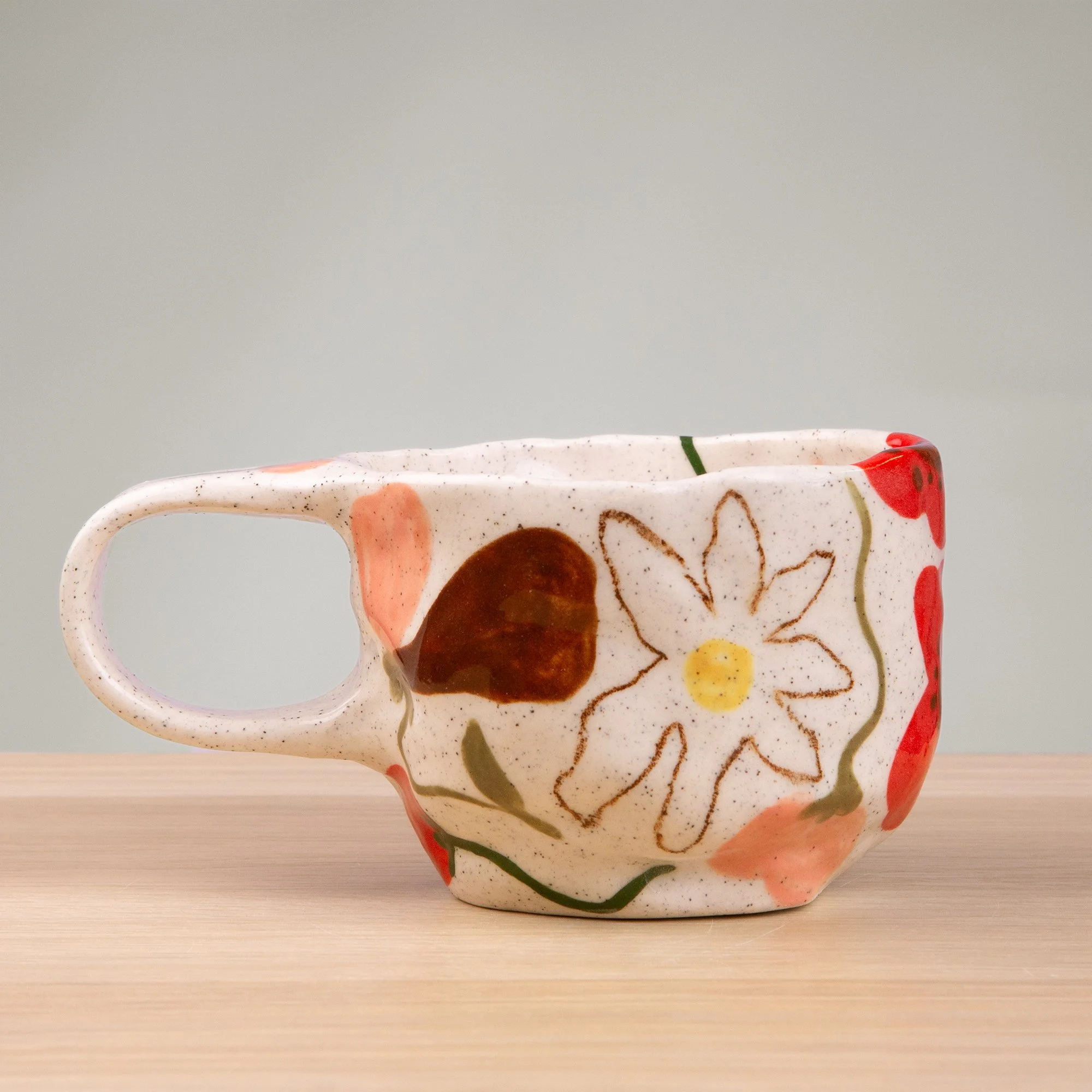 A soft garden in bloom, this handmade ceramic mug is adorned with hand-painted poppies, daisies and sweet pea flowers in a delicate, painterly style.