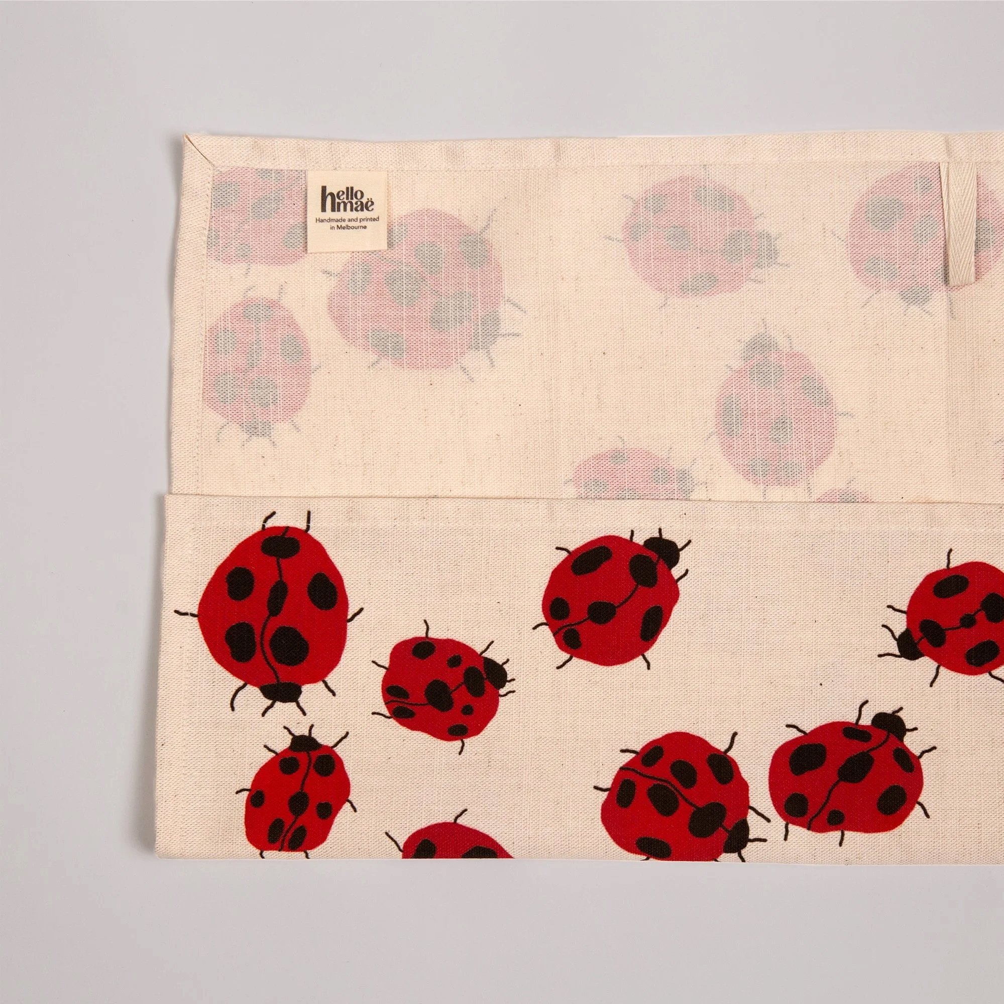 Colourful Loveliness tea towel featuring a playful print of red ladybugs and garden-inspired details.