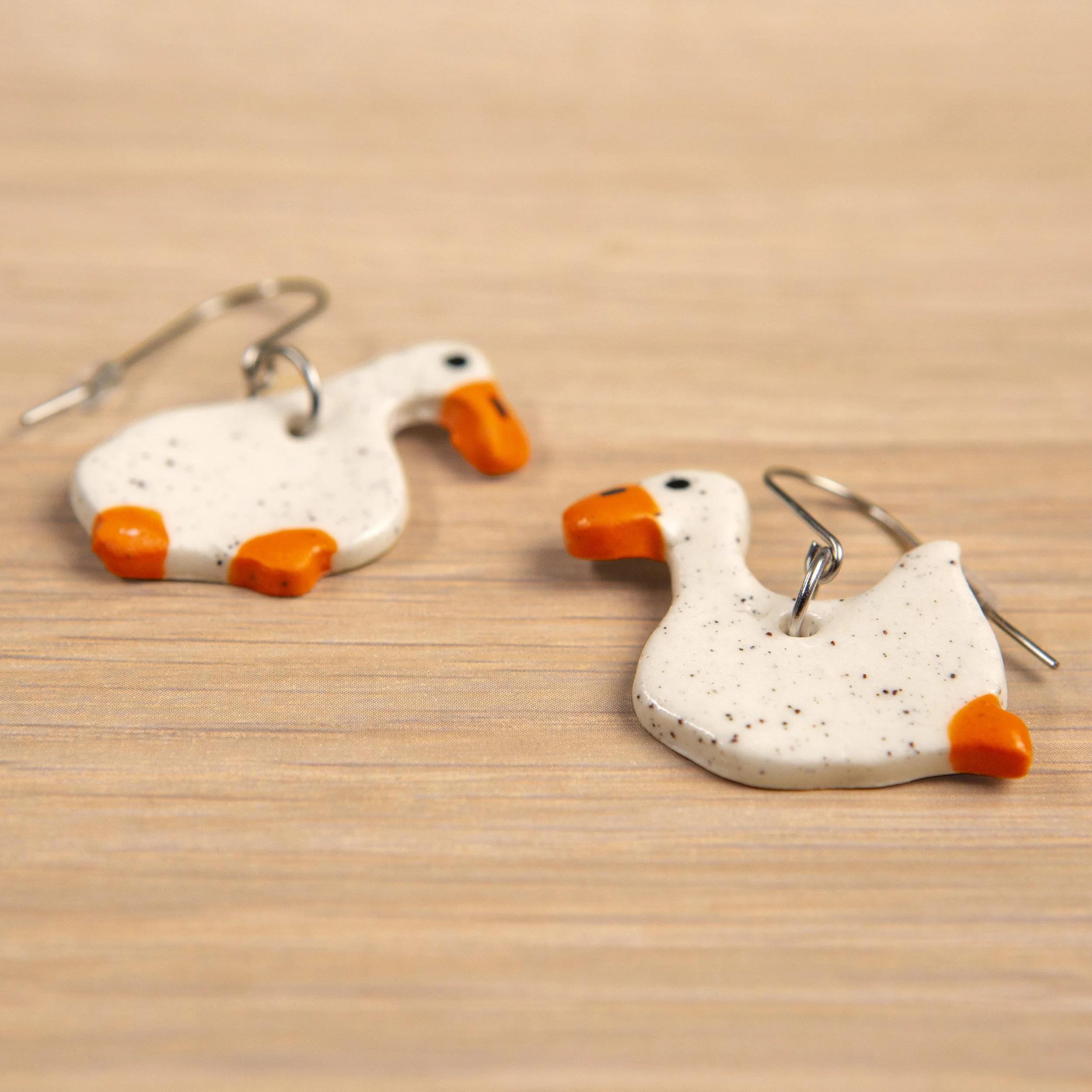 Handmade one-tier ceramic white mismatched duck earrings with surgical steel hooks photographed on a neutral background.