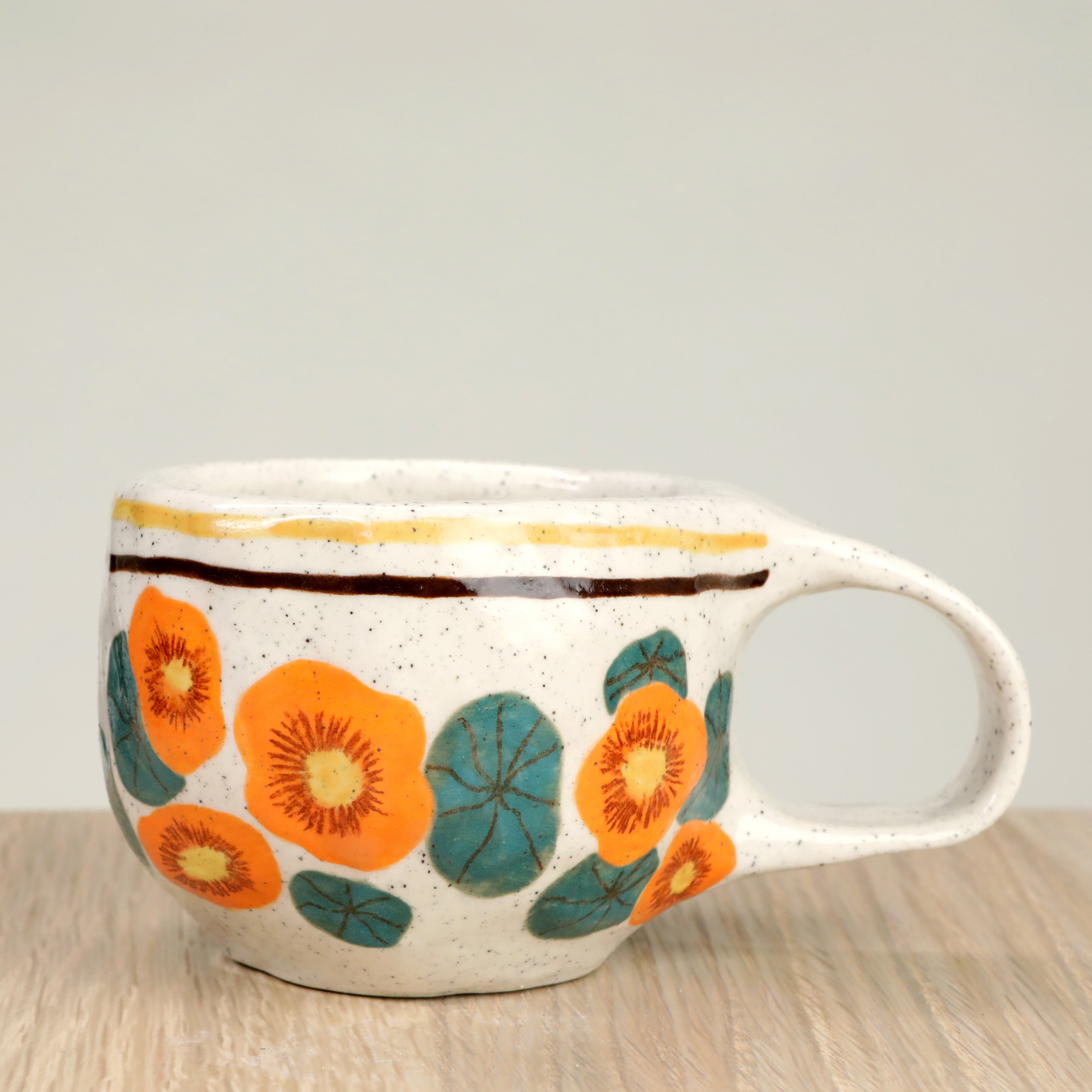 Handmade ceramic coffee cup with hand-painted nasturtium flowers & 2 lines border, crafted from speckled clay in Melbourne. Holds approximately 150ml.
