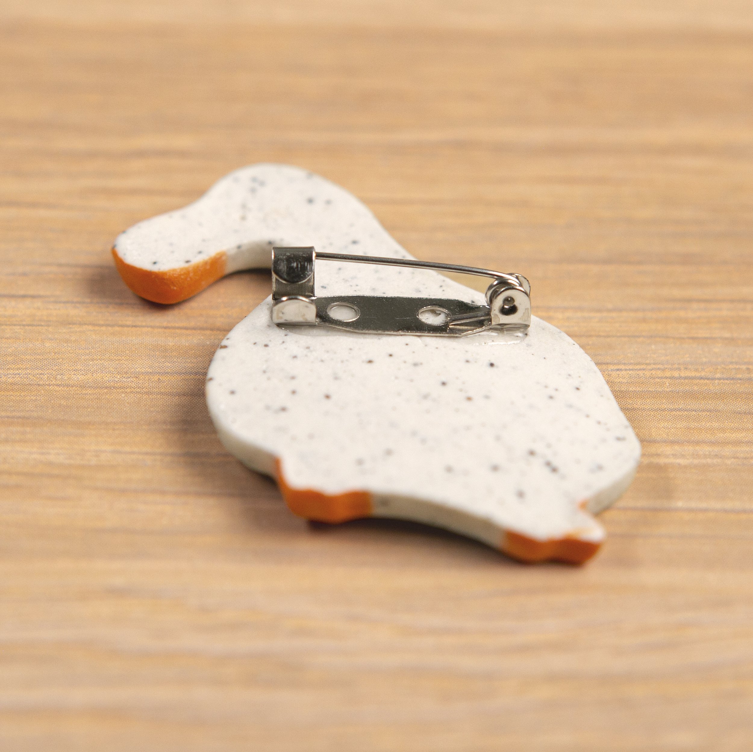 Handmade ceramic brooch with a glossy dreamer white duck, photographed on a neutral background
