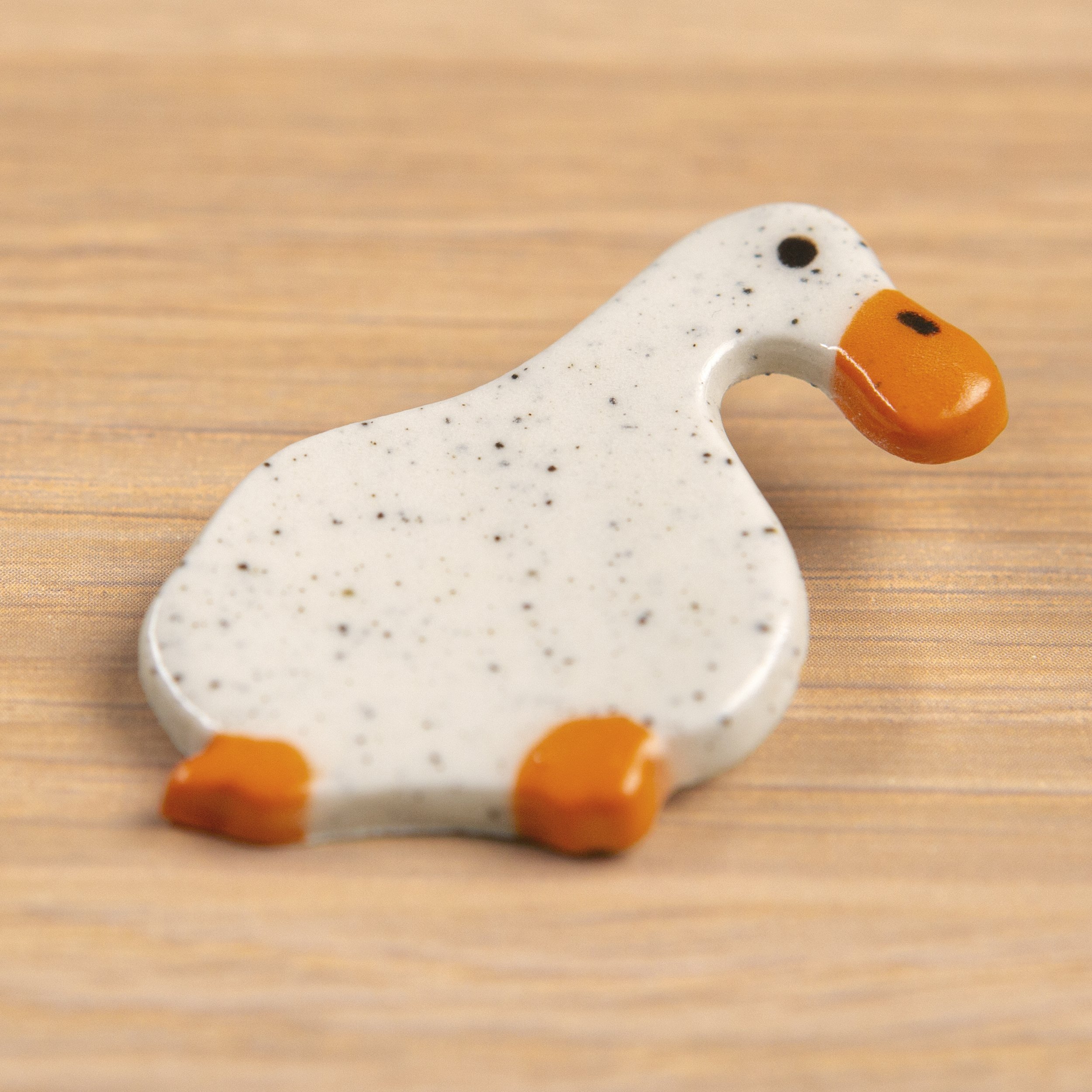 Handmade ceramic brooch with a glossy dreamer white duck, photographed on a neutral background