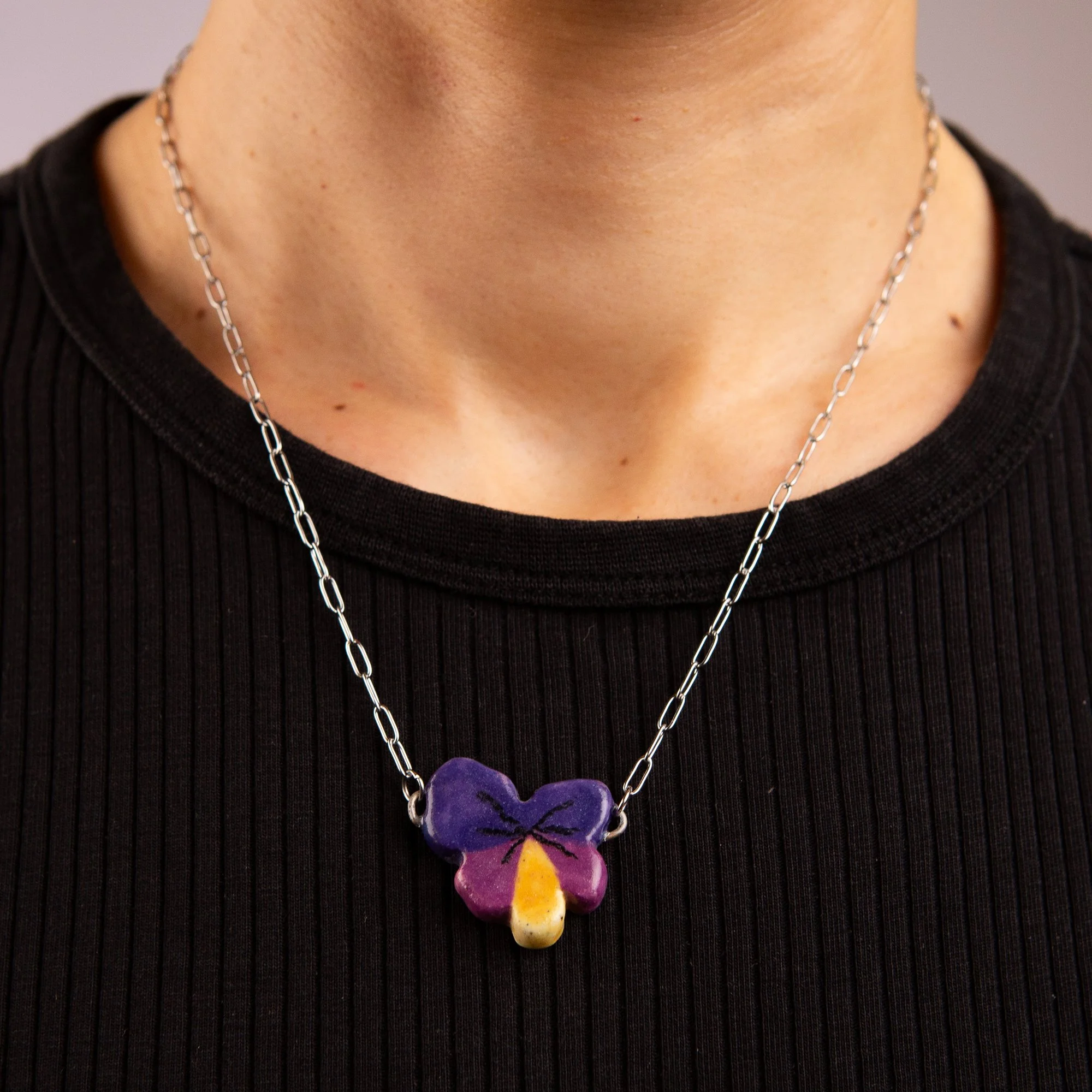 Handmade ceramic pansy necklace featuring a playful hand-painted pansy pendant on a silver-coloured chain.