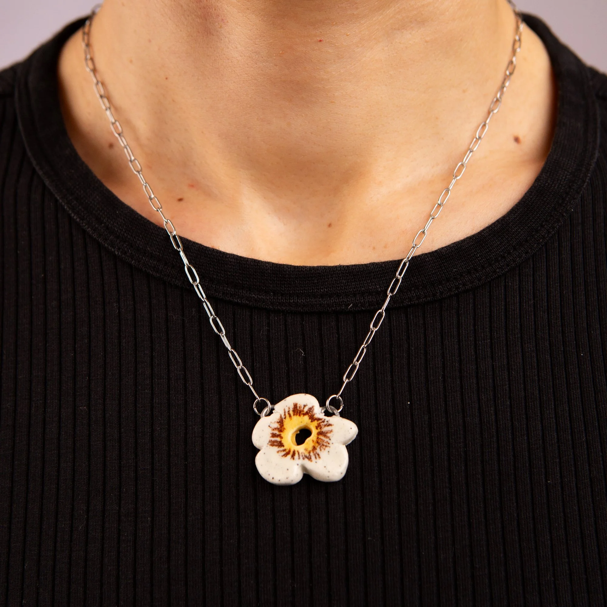 Handmade ceramic white flower necklace featuring a playful hand-painted white flower pendant on a silver-coloured chain.