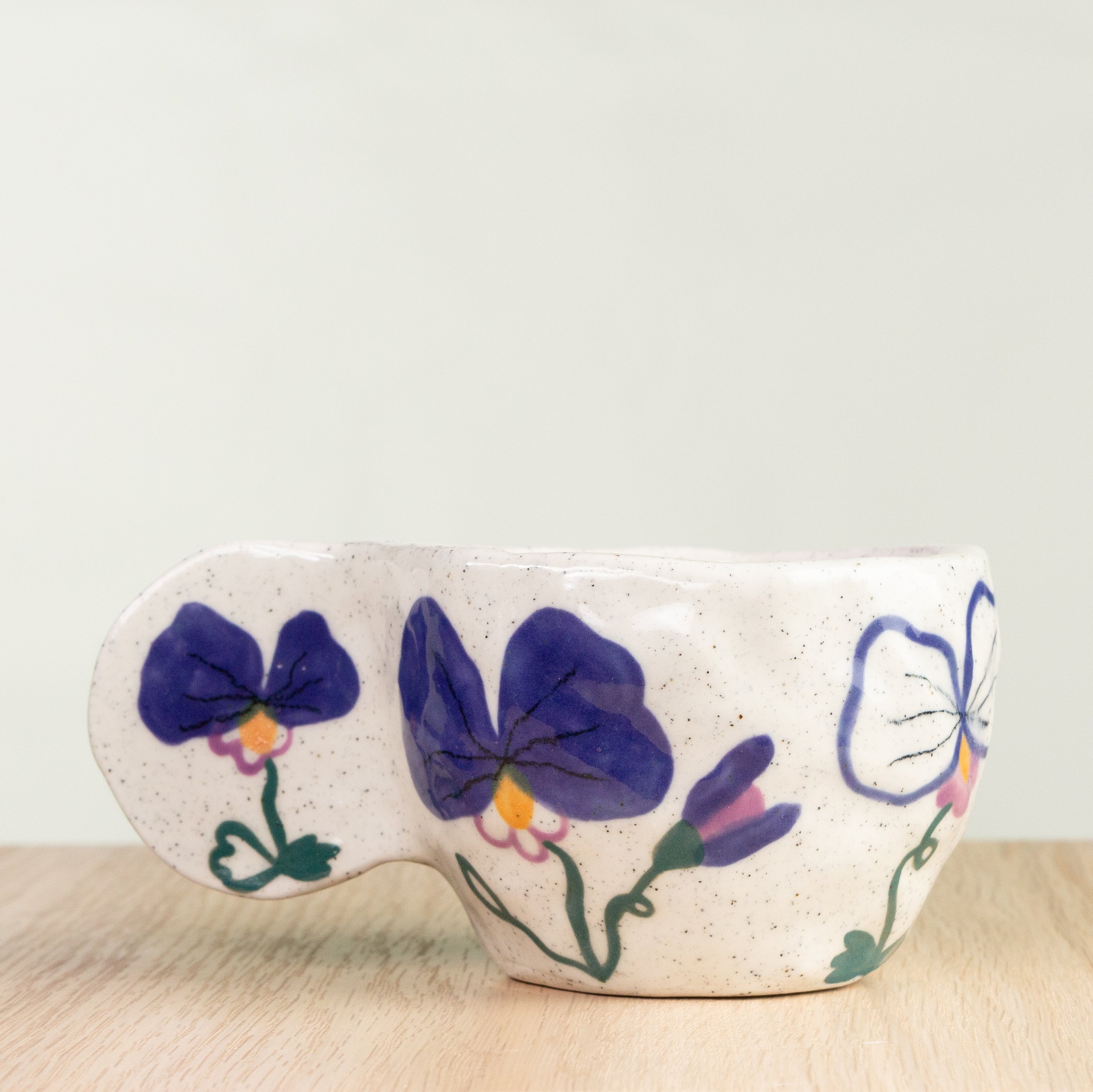 Handmade ceramic coffee cup with hand-painted pansy flowers, crafted from speckled clay in Melbourne. Holds approximately 150ml.