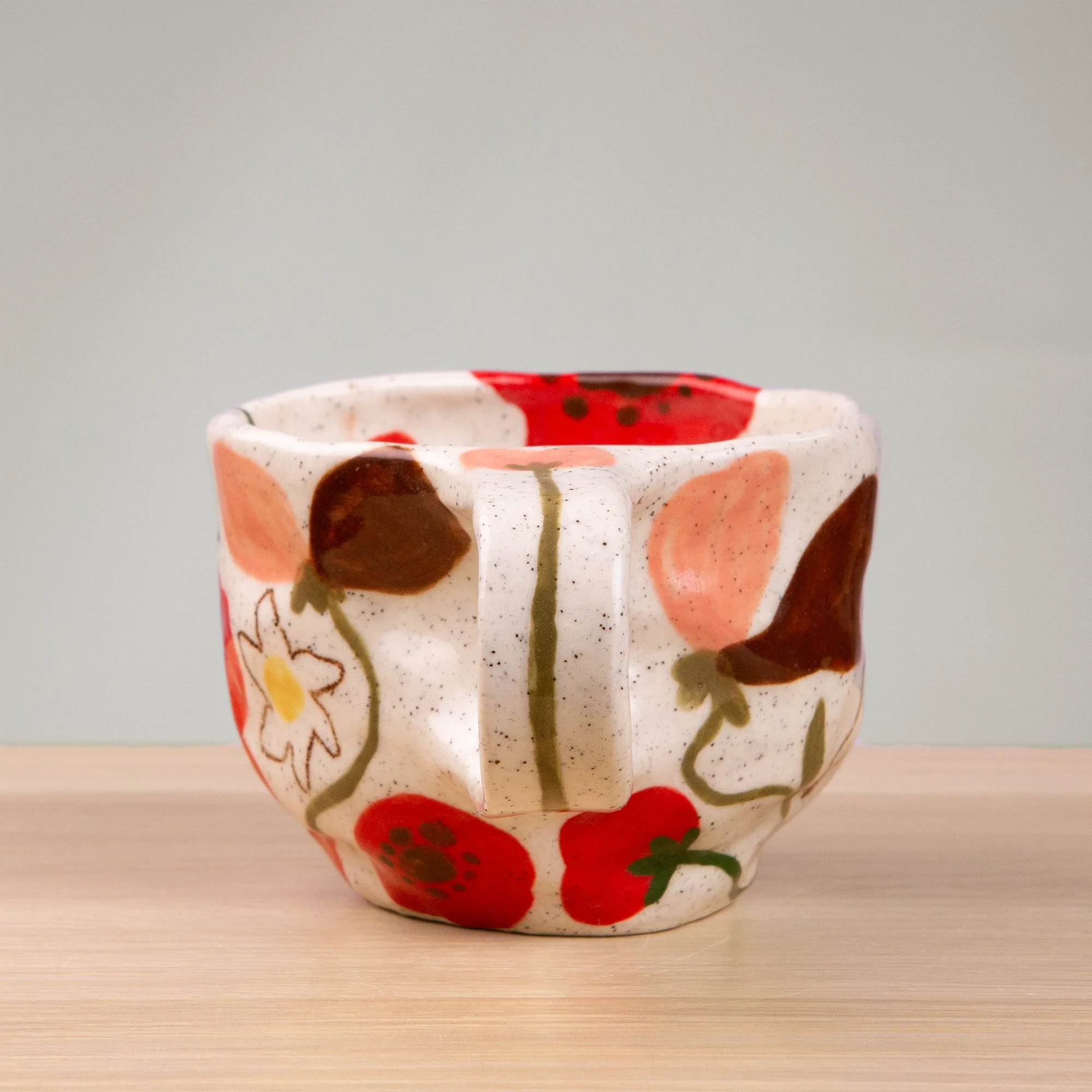 A soft garden in bloom, this handmade ceramic mug is adorned with hand-painted poppies, daisies and sweet pea flowers in a delicate, painterly style.