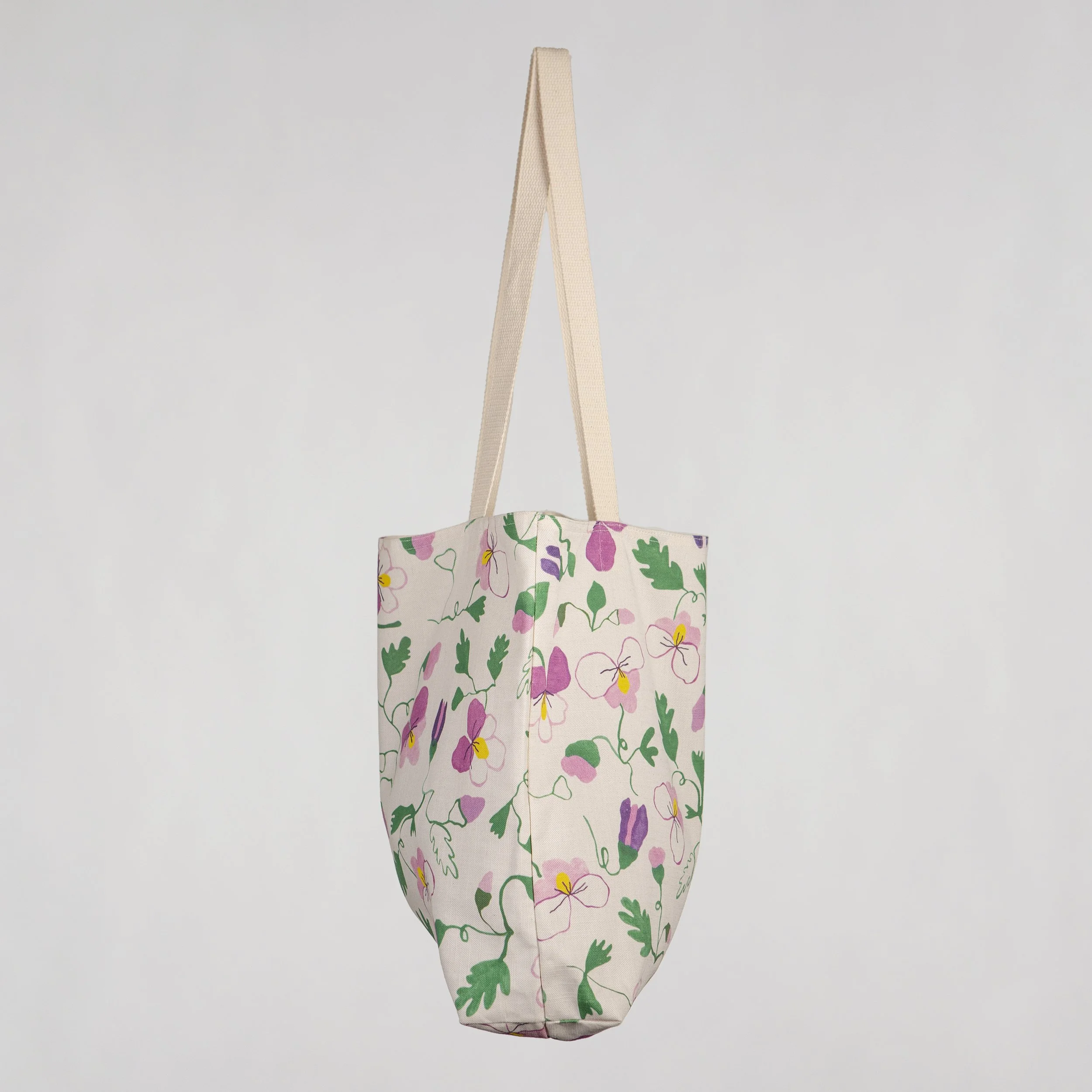 Cotton linen tote bag with a hand-drawn Pansy Flowers print, hanging on a wall. Soft, structured, and made in Melbourne.