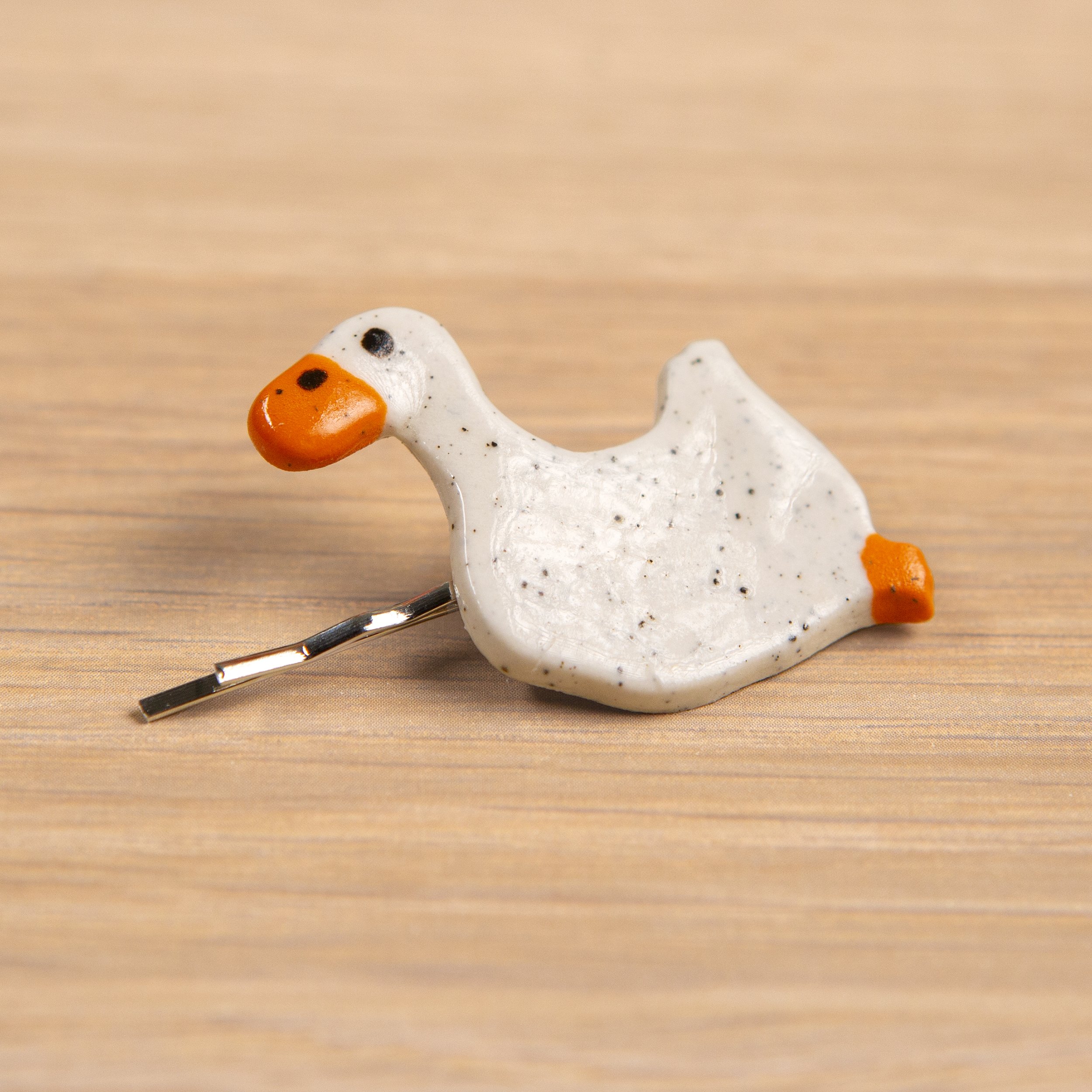 Handmade ceramic hair pin with a glossy swimming white duck, photographed on a neutral background.