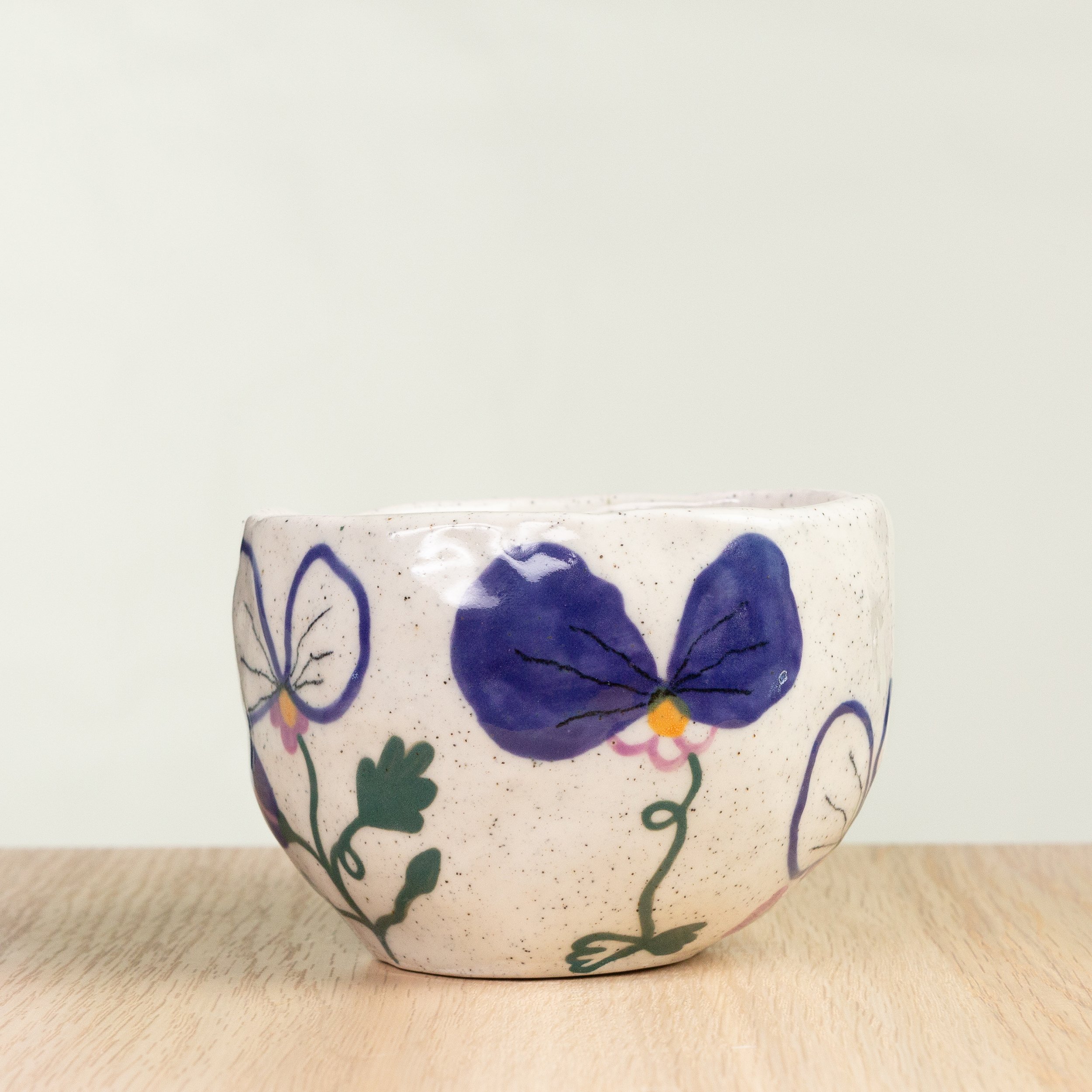 Handmade ceramic coffee cup with hand-painted pansy flowers, crafted from speckled clay in Melbourne. Holds approximately 300ml.