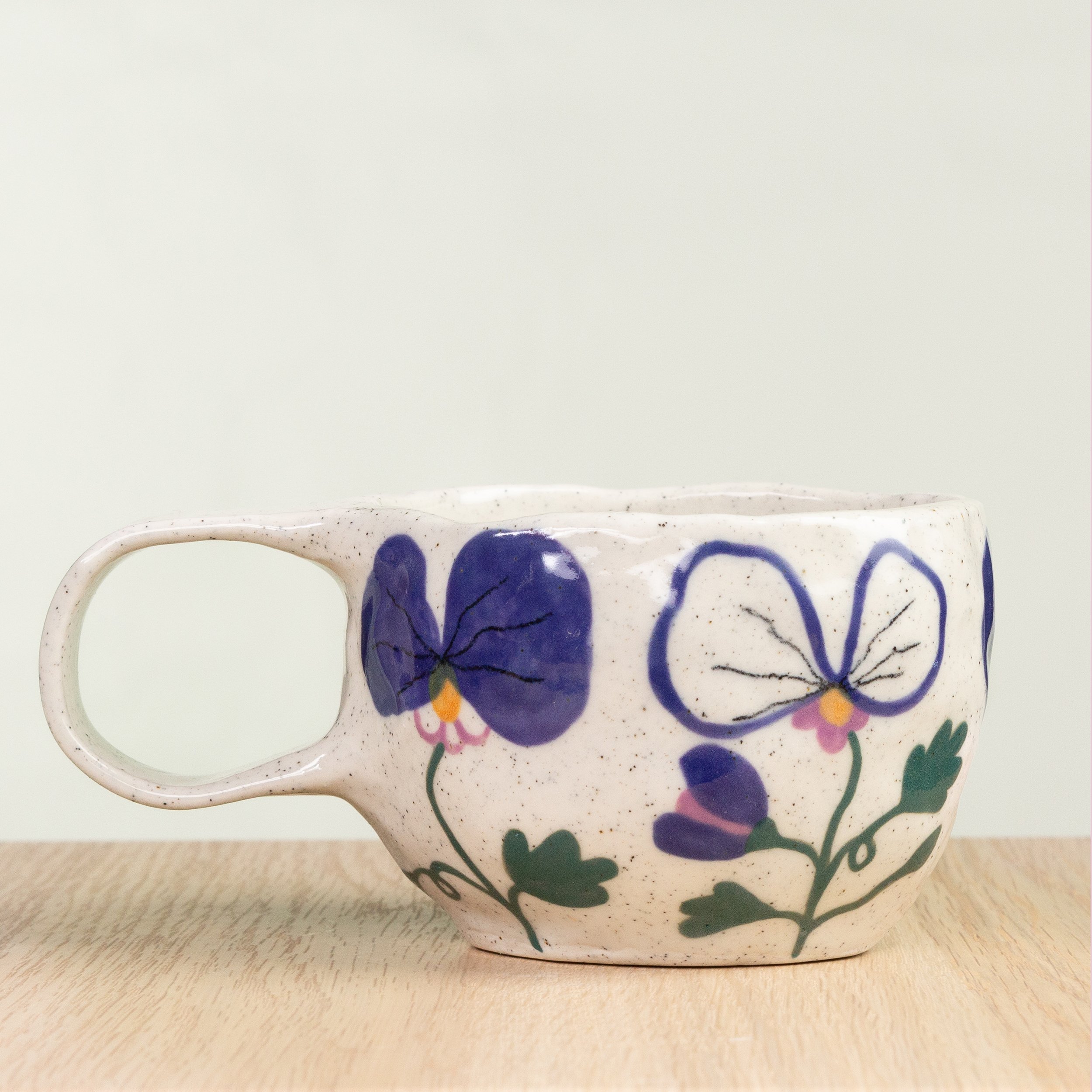 Handmade ceramic coffee cup with hand-painted pansy flowers, crafted from speckled clay in Melbourne. Holds approximately 150ml.