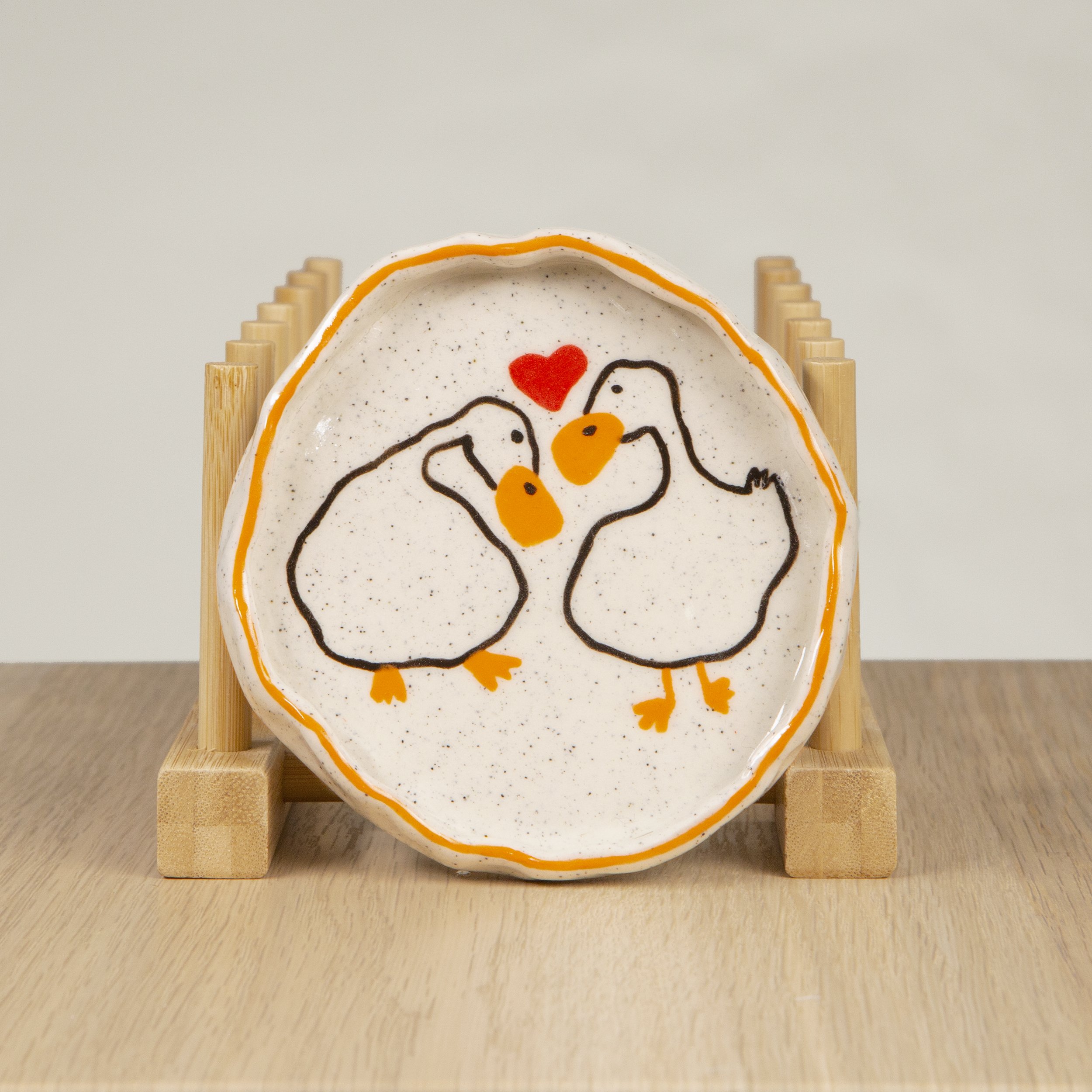 Round ceramic trinket dish featuring a hand-painted loving ducks & orange line border design on speckled clay, designed by hellomaë.