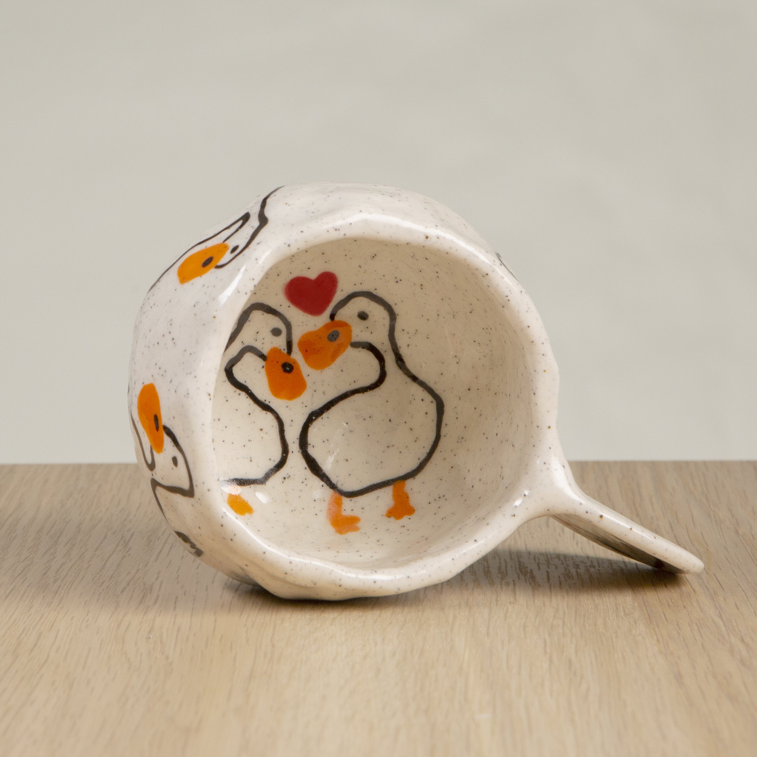 Handmade ceramic coffee cup with hand-painted loving ducks, crafted from speckled clay in Melbourne with a cute petal handle. Holds approximately 150ml.