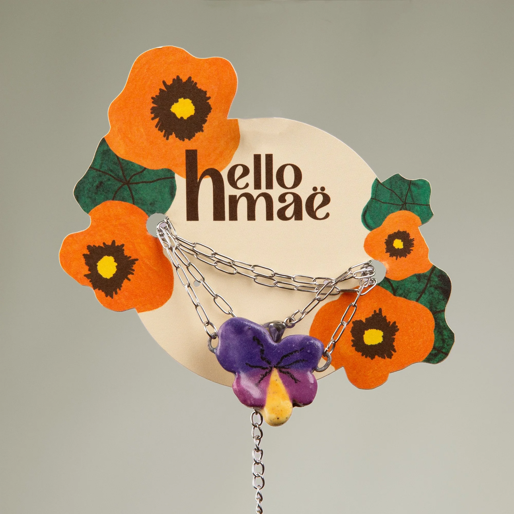 Handmade ceramic pansy necklace featuring a playful hand-painted pansy pendant on a silver-coloured chain.
