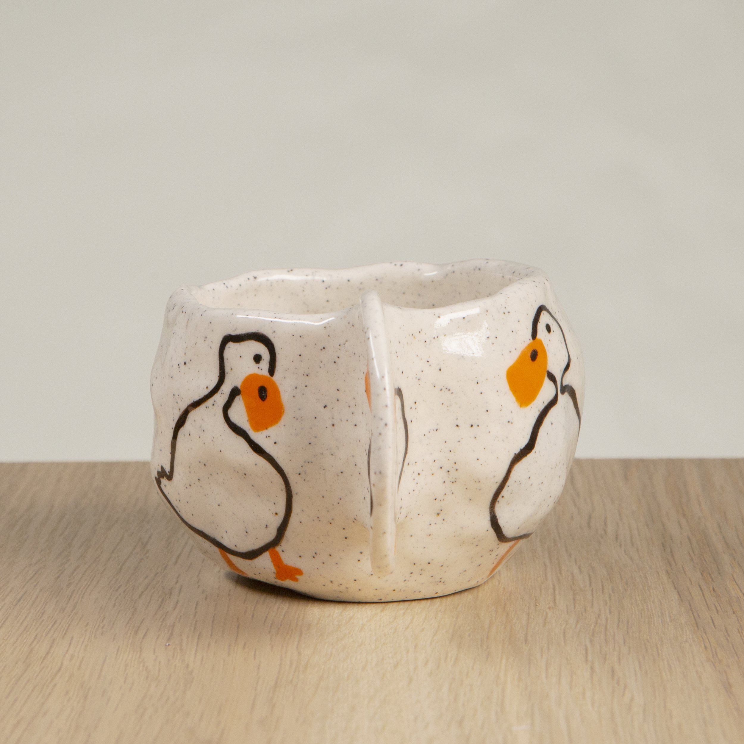 Handmade ceramic coffee cup with hand-painted loving ducks, crafted from speckled clay in Melbourne with a cute petal handle. Holds approximately 150ml.
