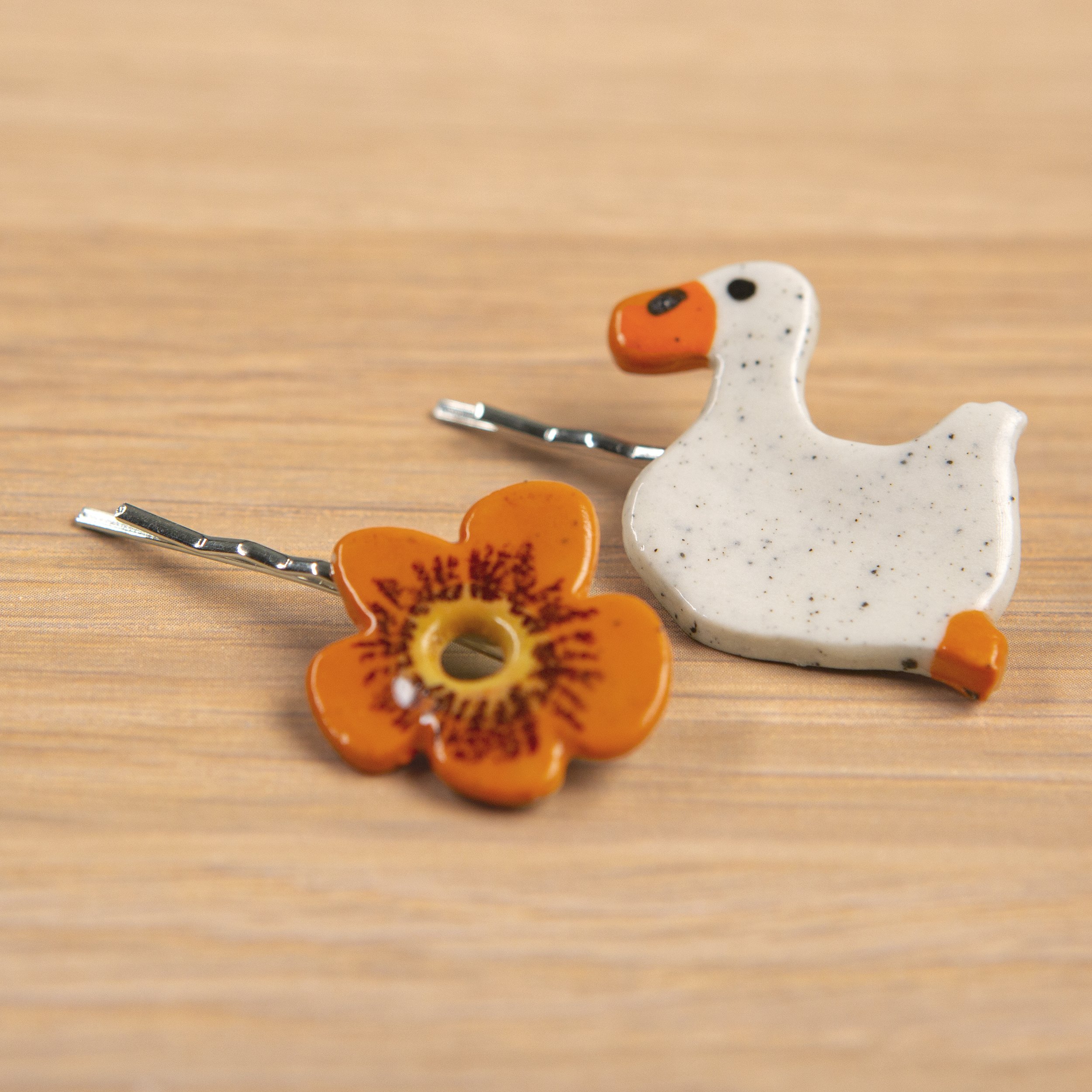 A set of two ceramic hair pins – one orange flower and the other a swimming white duck, handmade and painted.