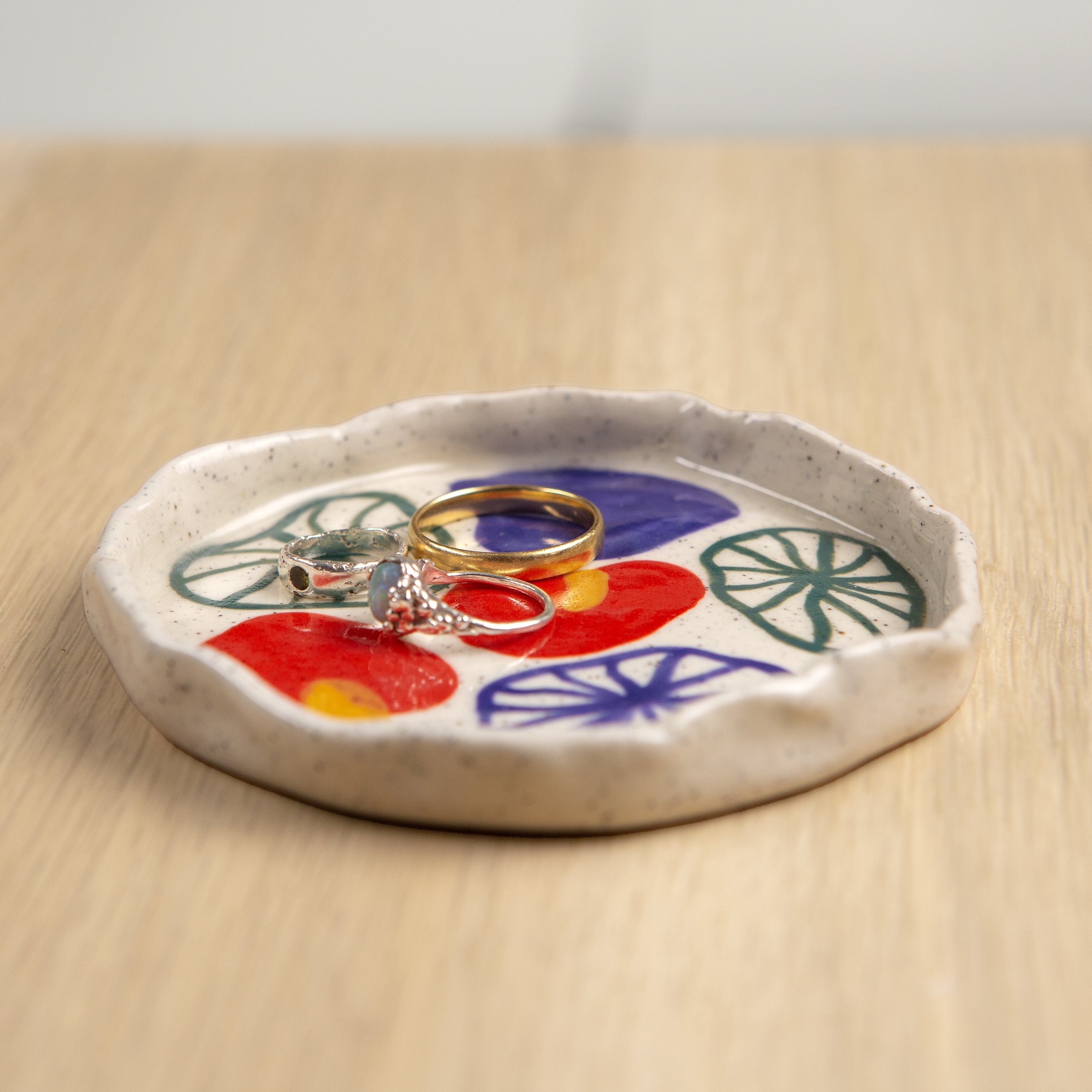 Round ceramic trinket dish featuring a hand-painted anthurium flower design on speckled clay, designed by hellomaë.