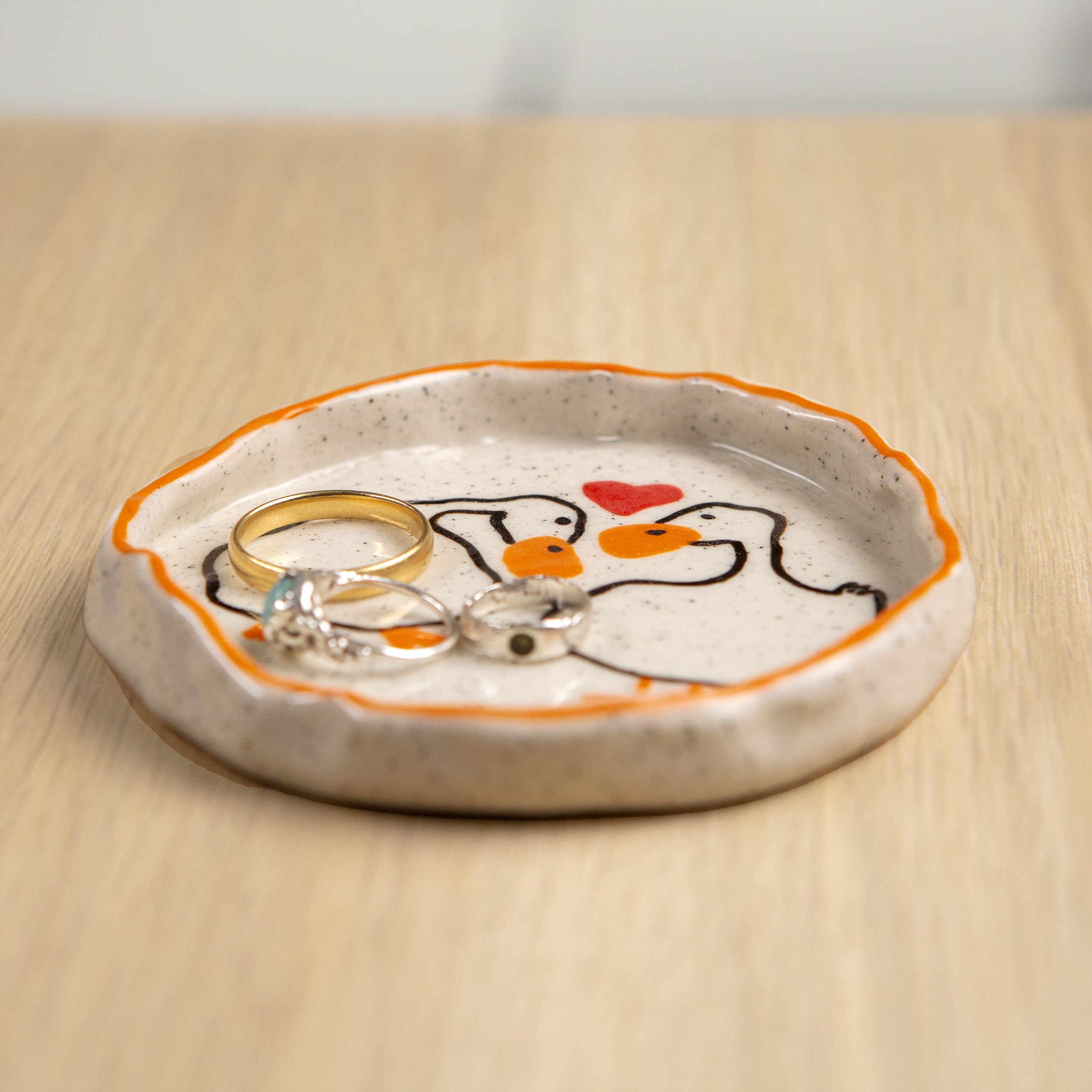Round ceramic trinket dish featuring a hand-painted loving duck & orange line border design on speckled clay, designed by hellomaë.