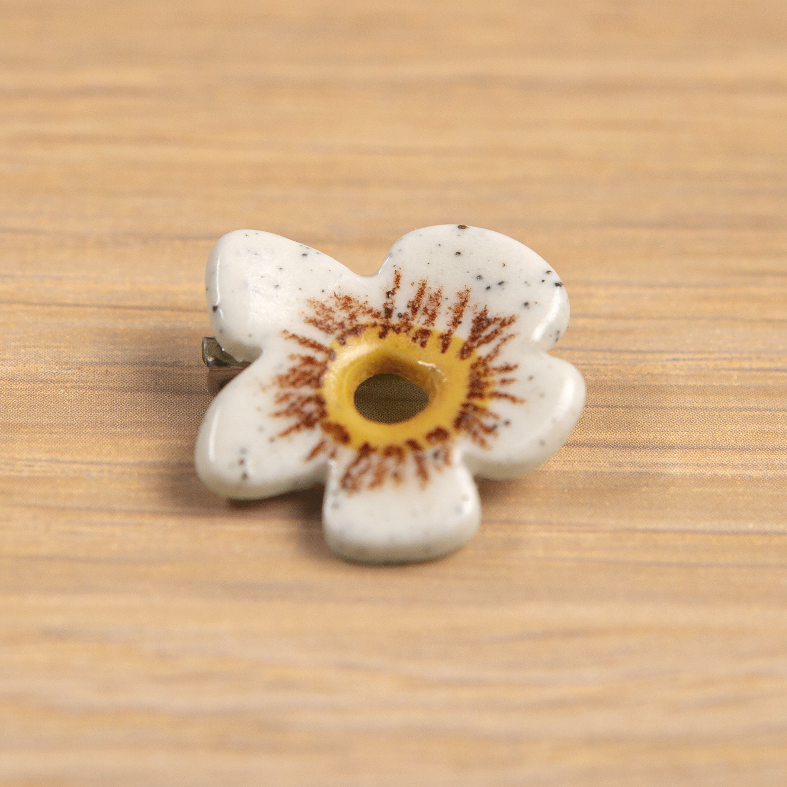 Handmade ceramic brooch with a glossy white flower, photographed on a neutral background