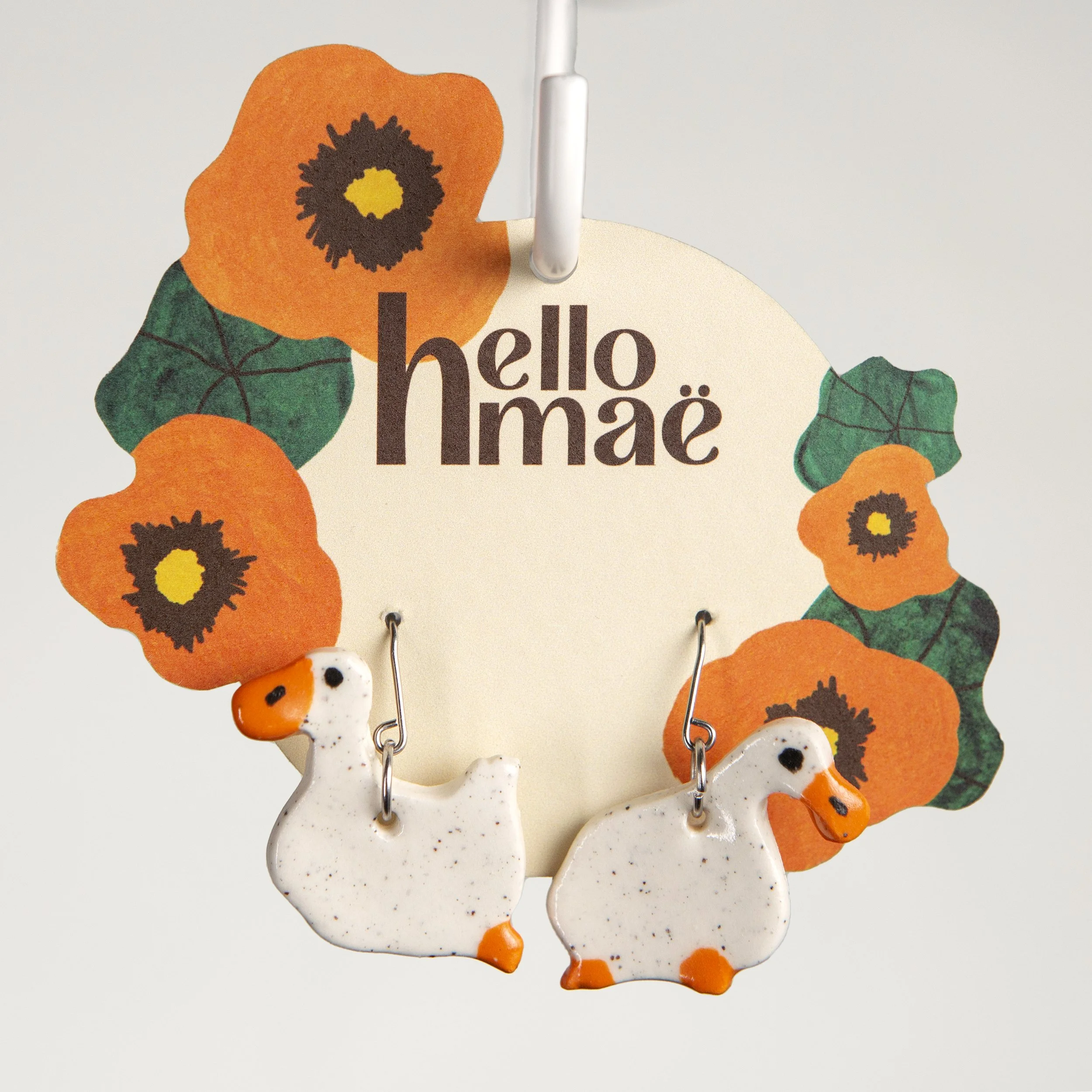 Handmade one-tier ceramic white mismatched duck earrings with surgical steel hooks photographed on a neutral background.