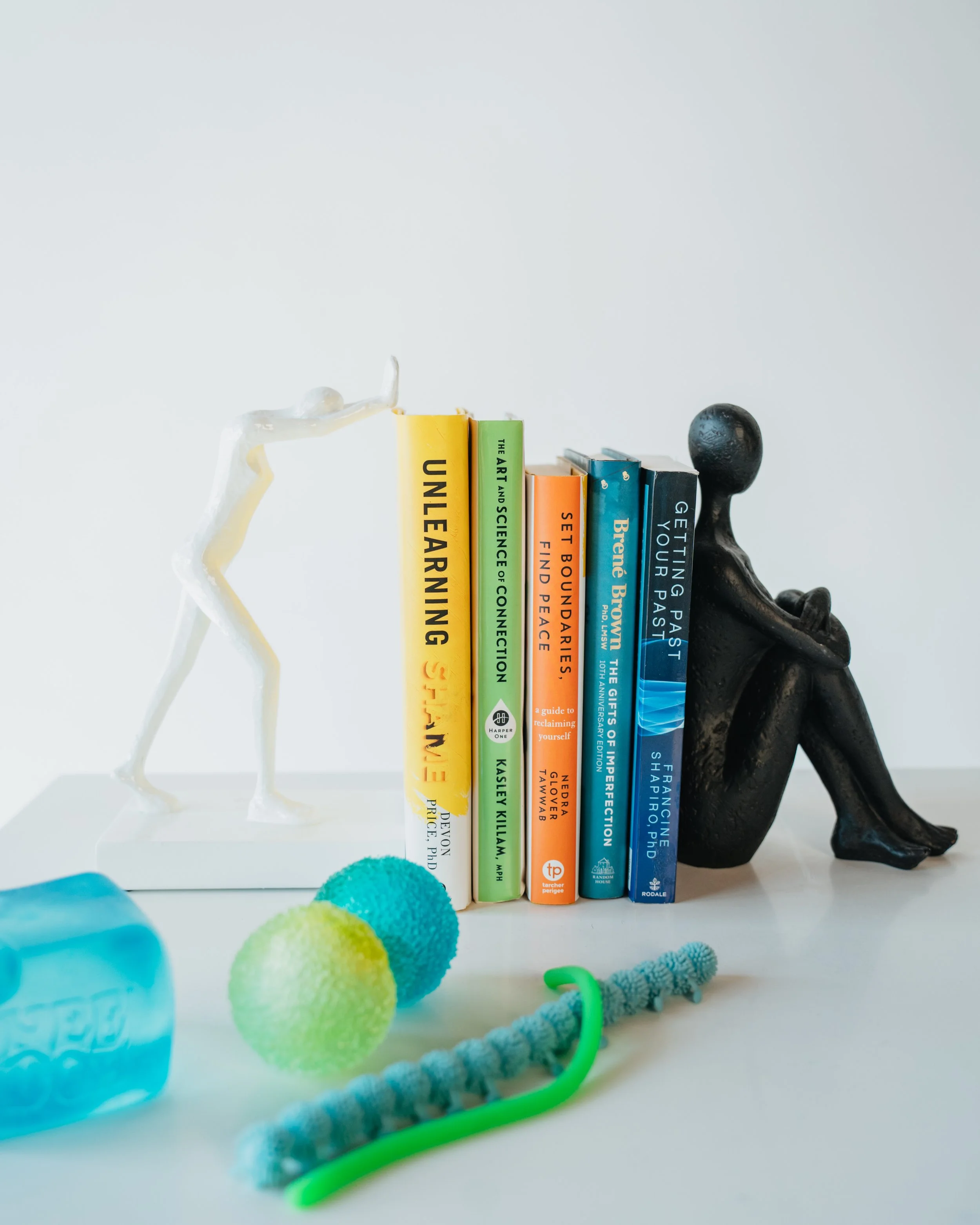 Therapy books, expressive sculptures, and colorful sensory tools representing the experiential and neurodivergent-affirming resources used at Ammonite Counseling.
