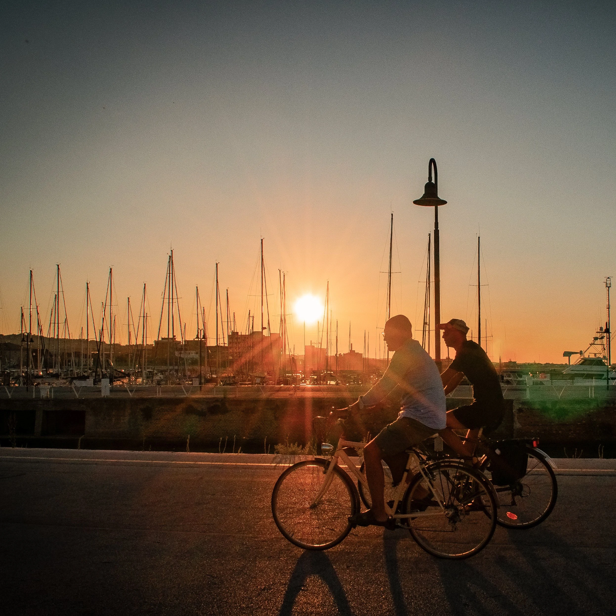 sunest in italy with two people cycling near a marina in senigallia le marche