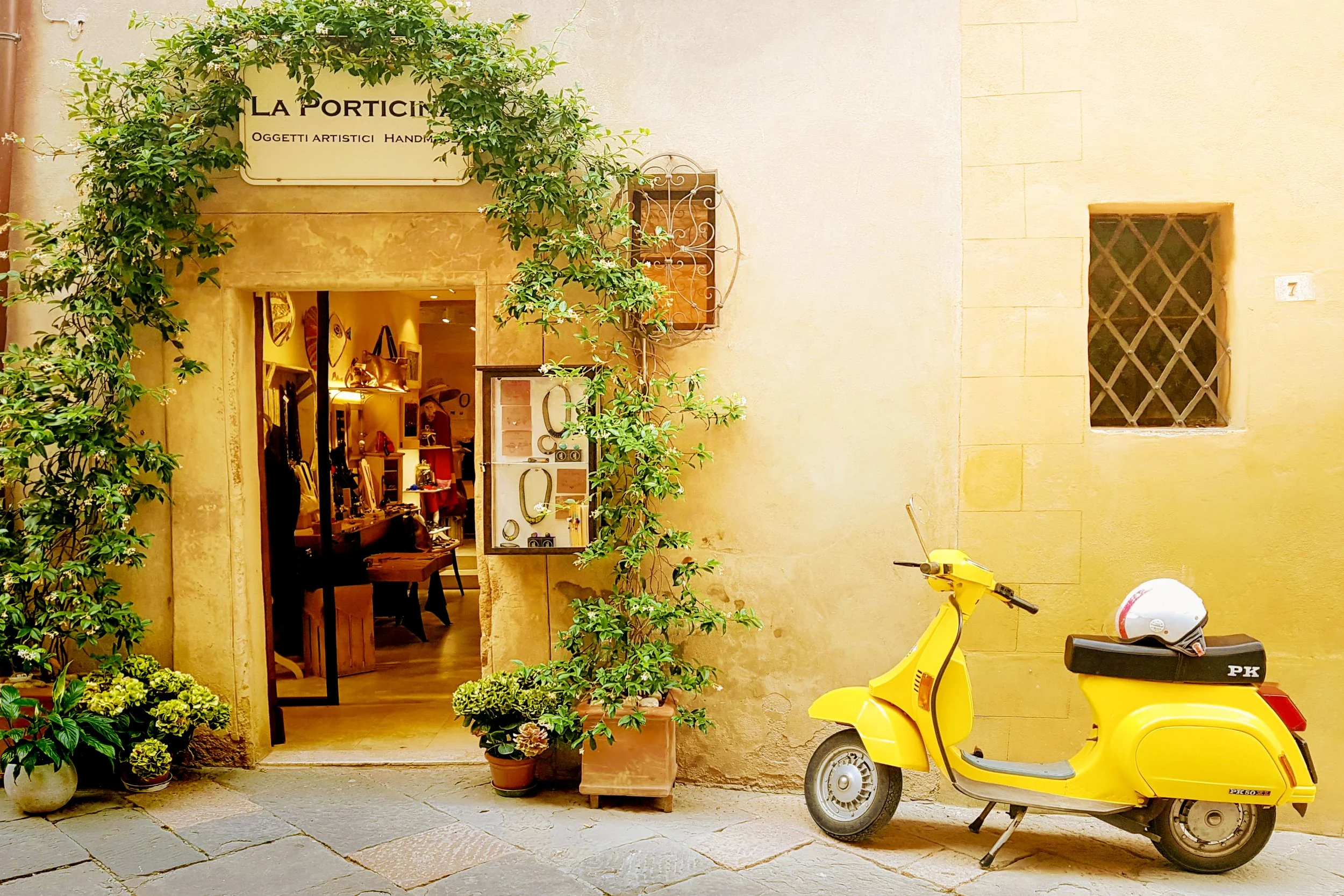 retro and classic yellow vespa with a white helmet perched on its seatparked outside of an italian book shop in rome