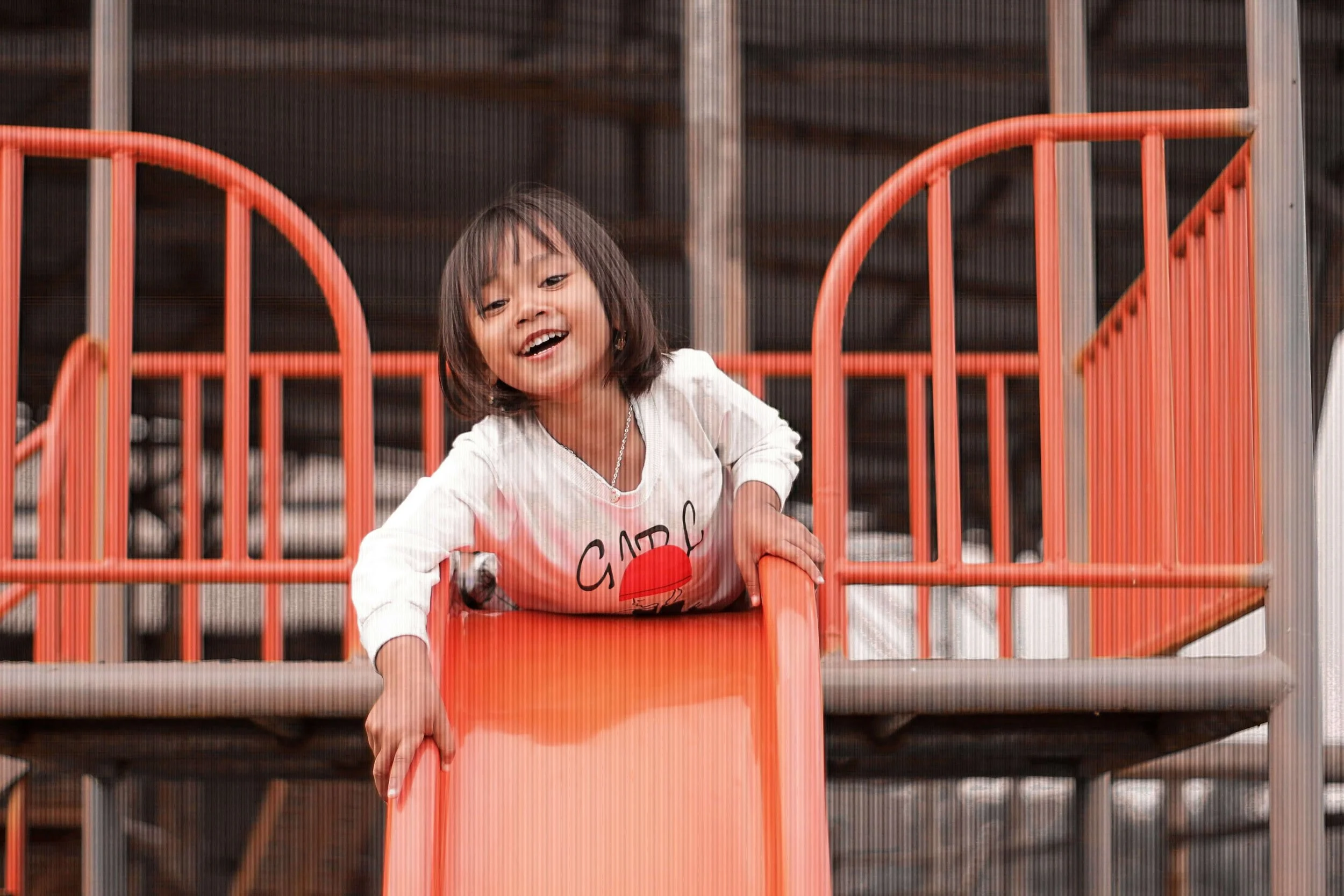 A young girl laughs while climbing up an orange playground slide. What are some fun summer ideas for kids in Arcadia? A family therapist in Arcadia, CA can help parents build stronger bonds through simple outdoor play.