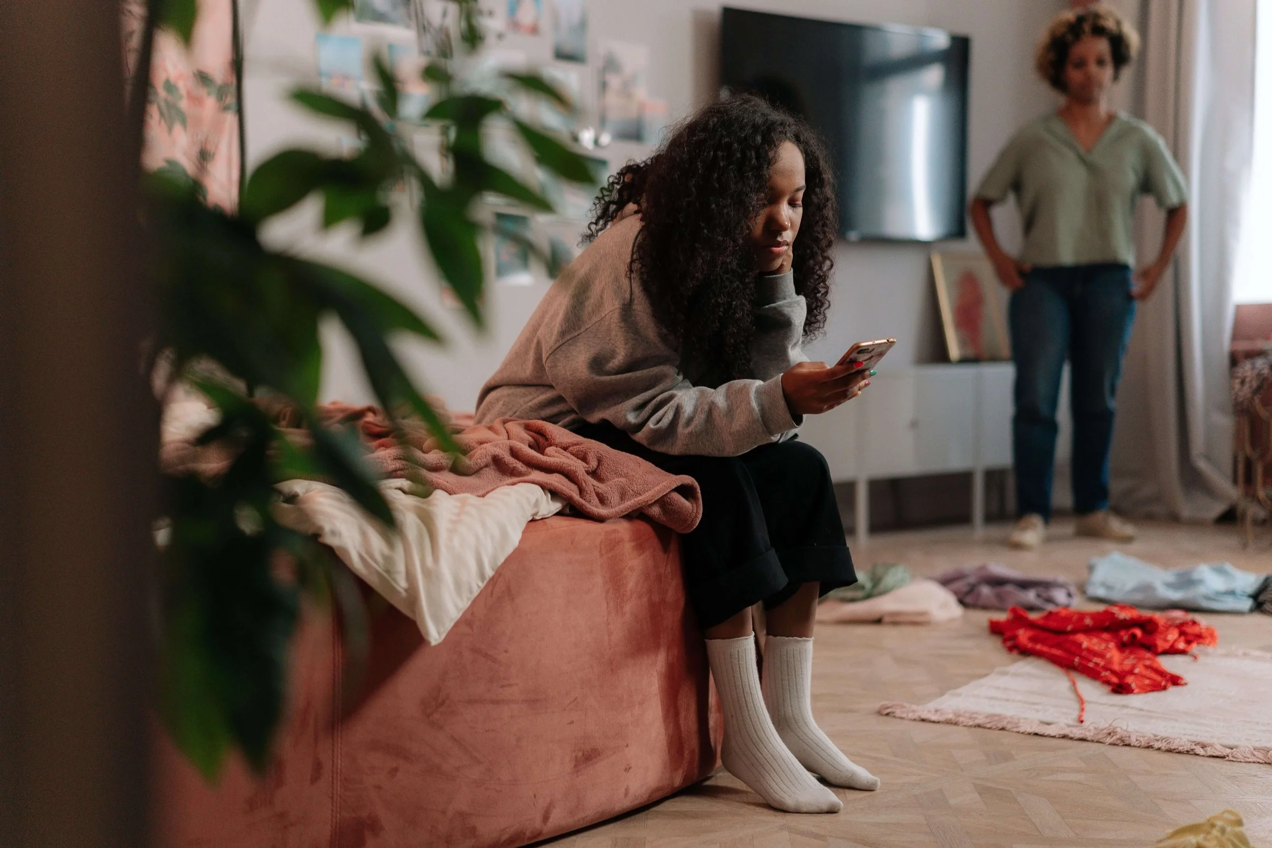 A teen girl sits looking at her phone while her mother stands watching from across the room. How do power dynamics shift as teens seek more independence? Family therapy in Arcadia, CA can help families navigate this changing relationship.