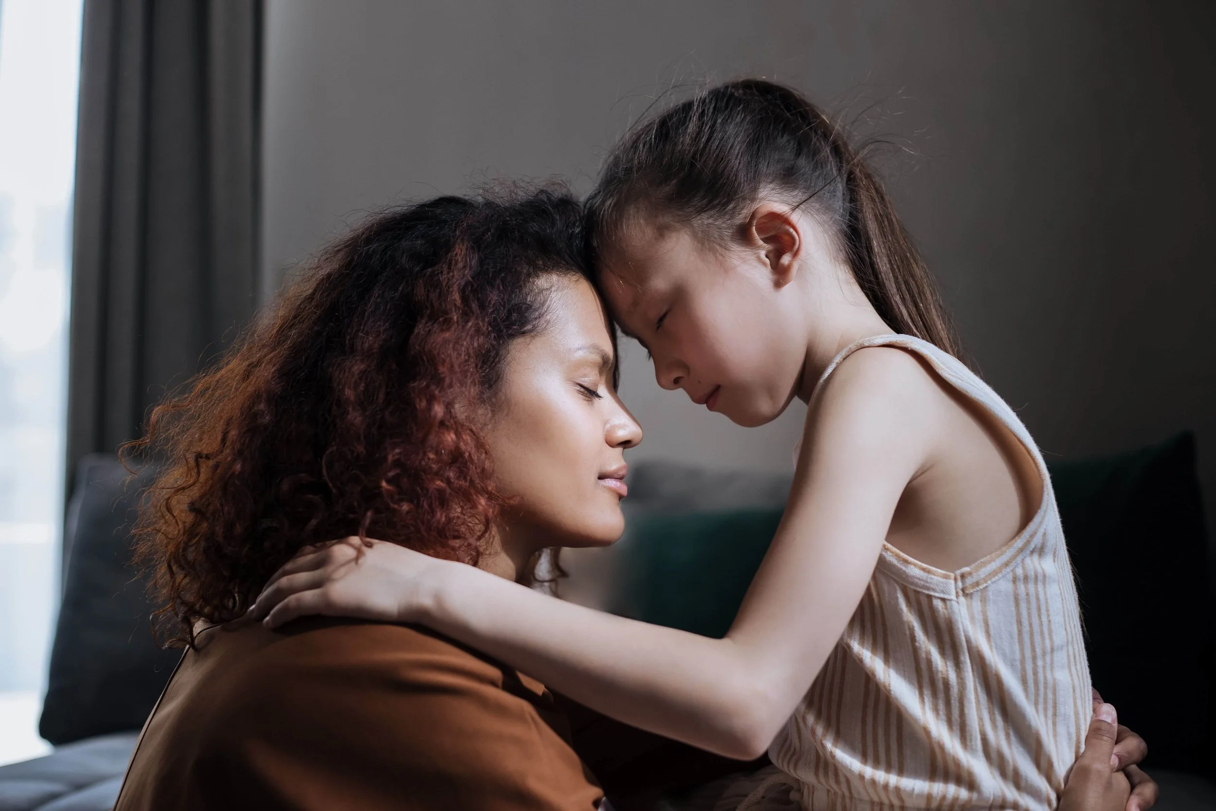 A mother and daughter sharing a comforting moment with their eyes closed and foreheads touching.