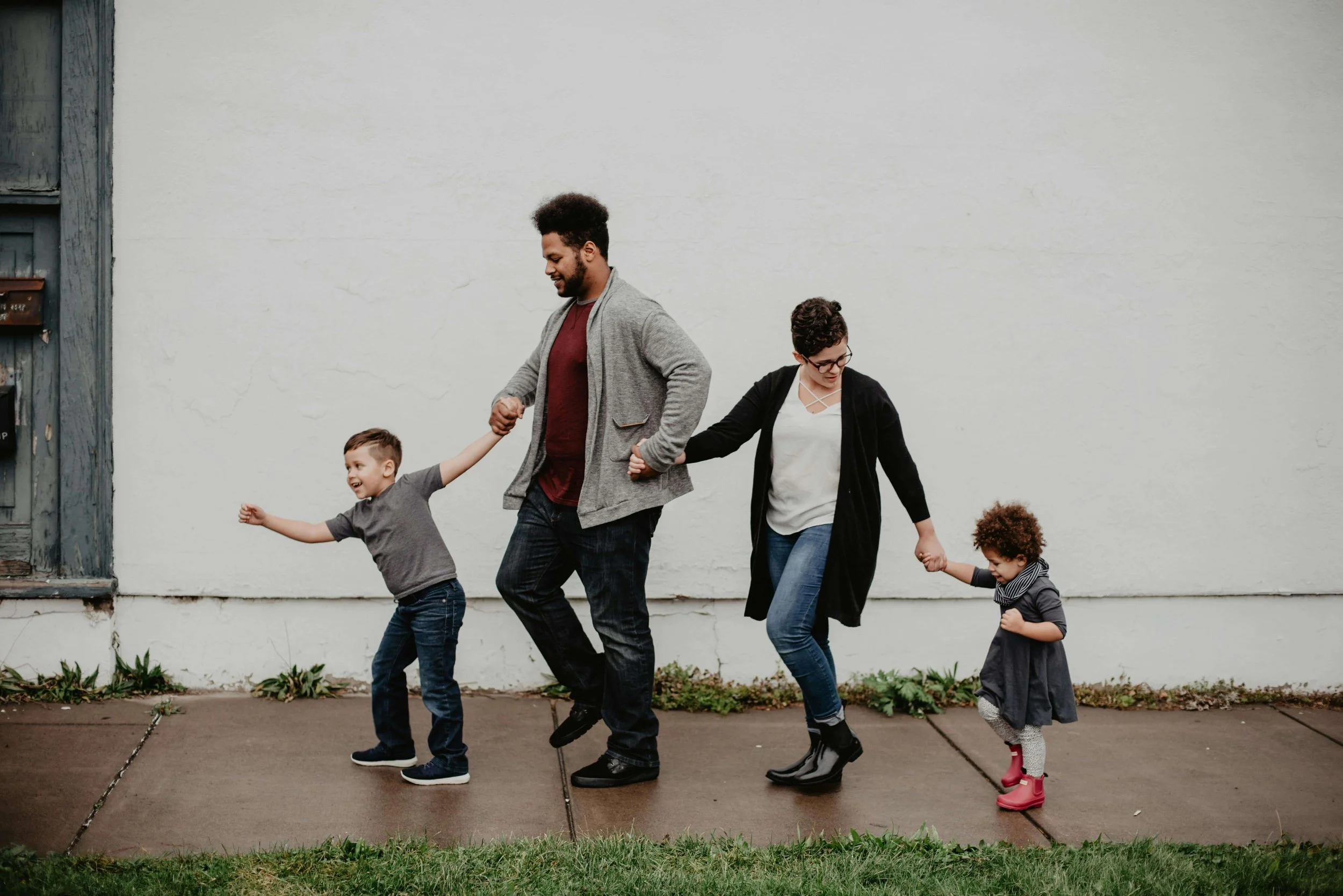 A joyful family of four walks hand in hand along a sidewalk, laughing together. When parents align on parenting, children thrive emotionally and feel more secure at home. Couples therapy in Arcadia, CA can help your family get there.