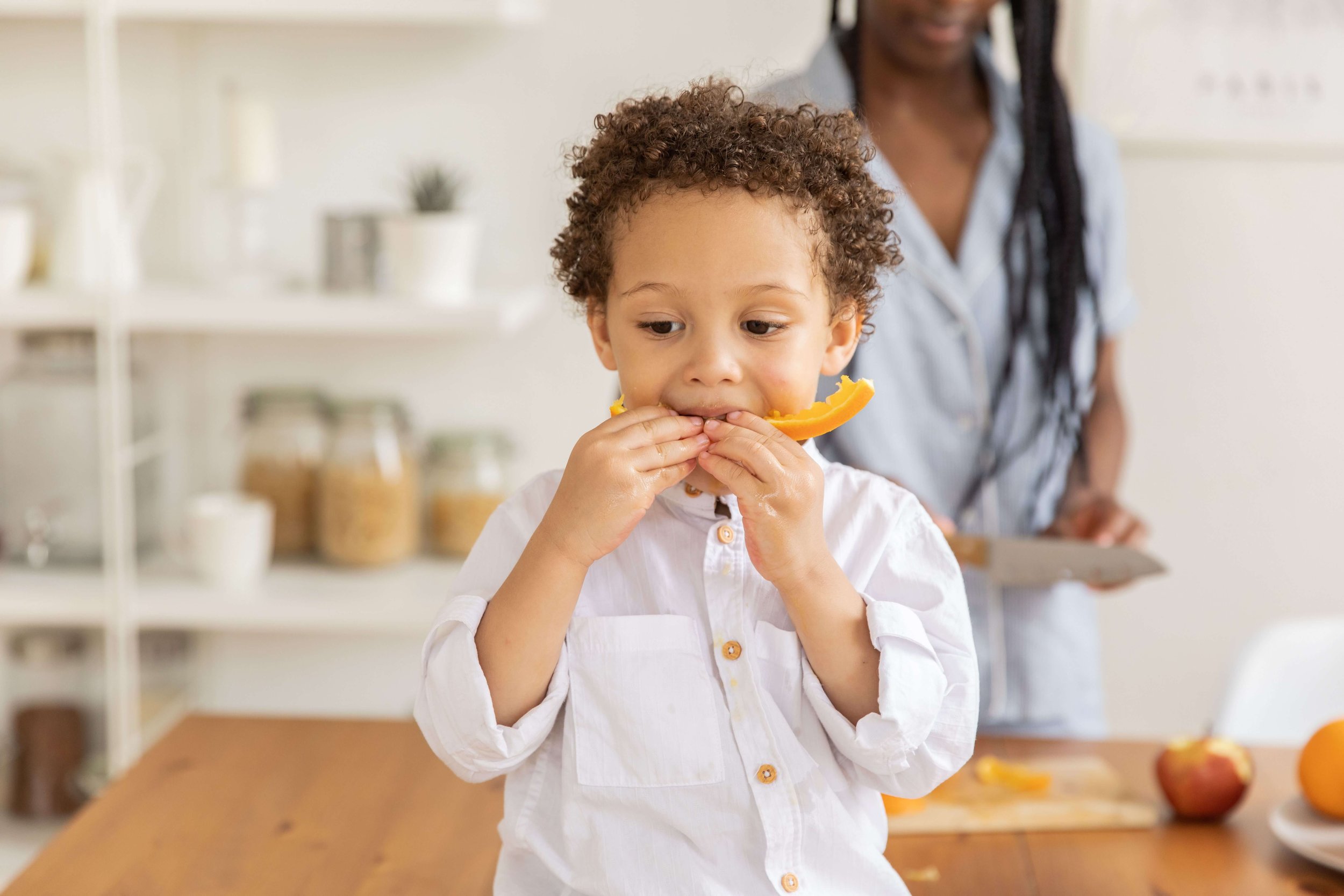 A child sitting at a table eating a piece of fruit.
