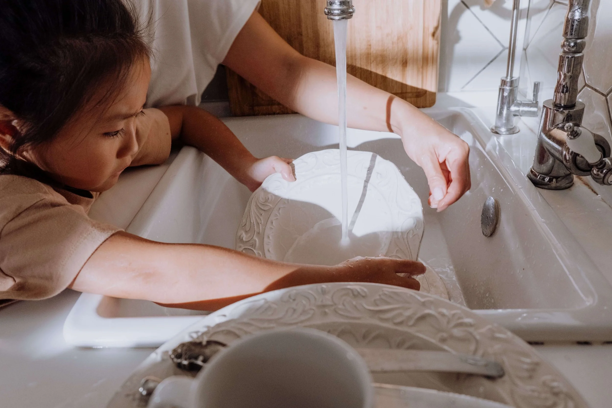 A young child washes dishes at the kitchen sink. What does an exhausted mother's daily load really look like? Family therapy in Arcadia, CA can help families notice and begin to share these invisible tasks.