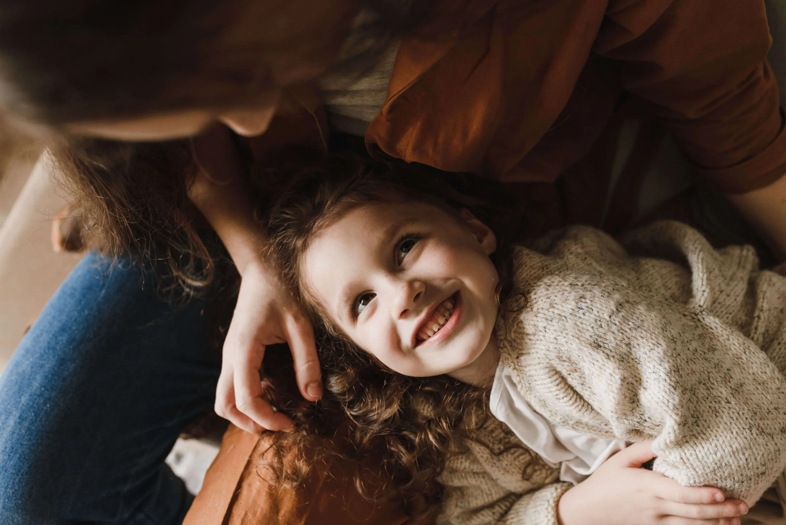 A young girls lied on her mother's lap while looking up at her and smiling.