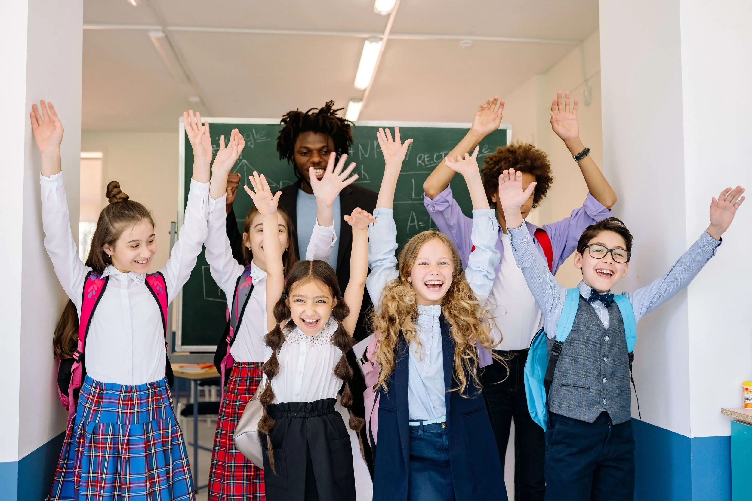 Children smile and raise their arms while standing in a school classroom.