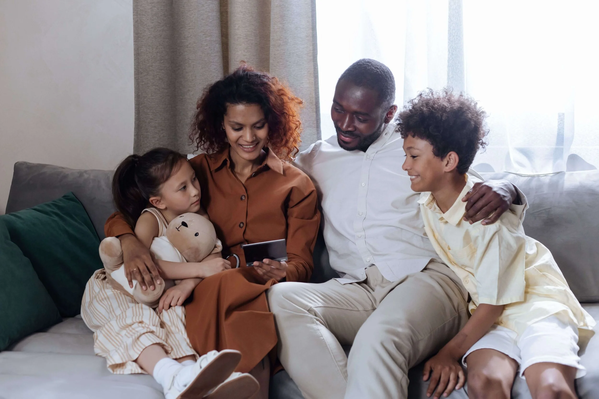A blended family of four snuggles on a couch. Are you a parent in a high-achieving family wondering whether your support has quietly shifted into pressure? A family therapist in Arcadia, CA, can help you navigate that line.
