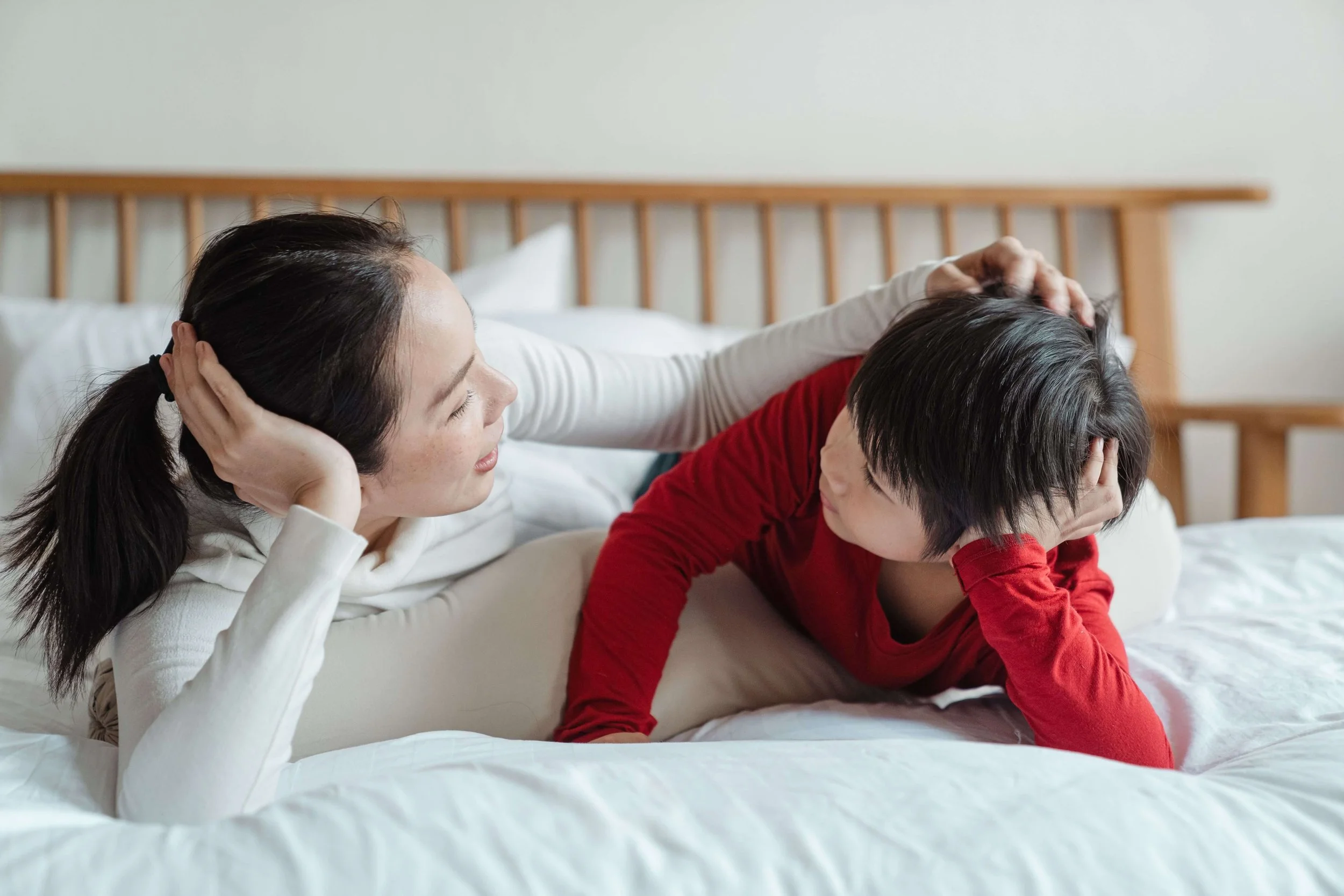 A mother talks to her young sone while they lie in bed facing each other.