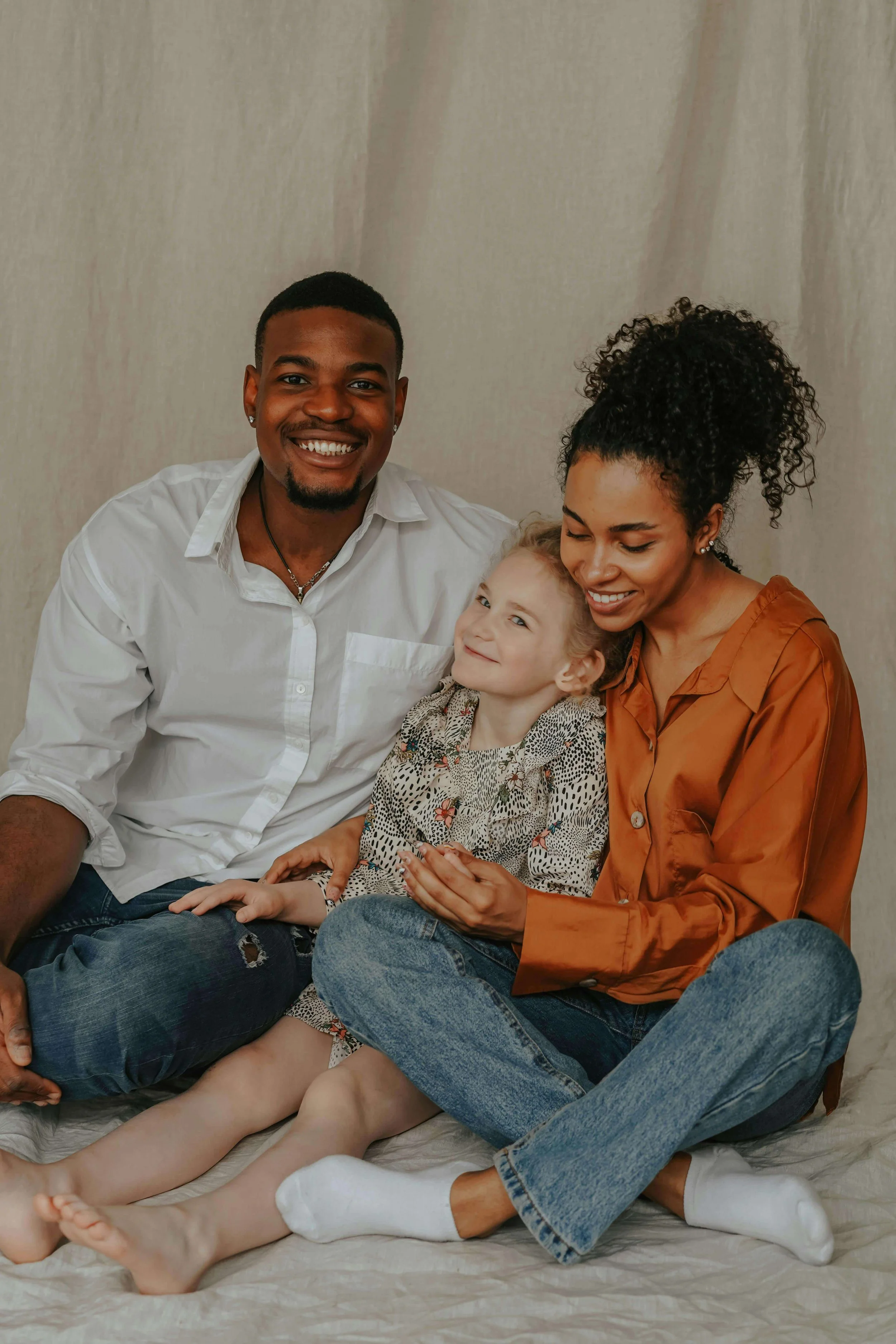 Parents sit closely with their young daughter between them, smiling together. The family demonstrates warmth and unity. A family therapist in Arcadia, CA, supports parents and children in building healthier relationships.