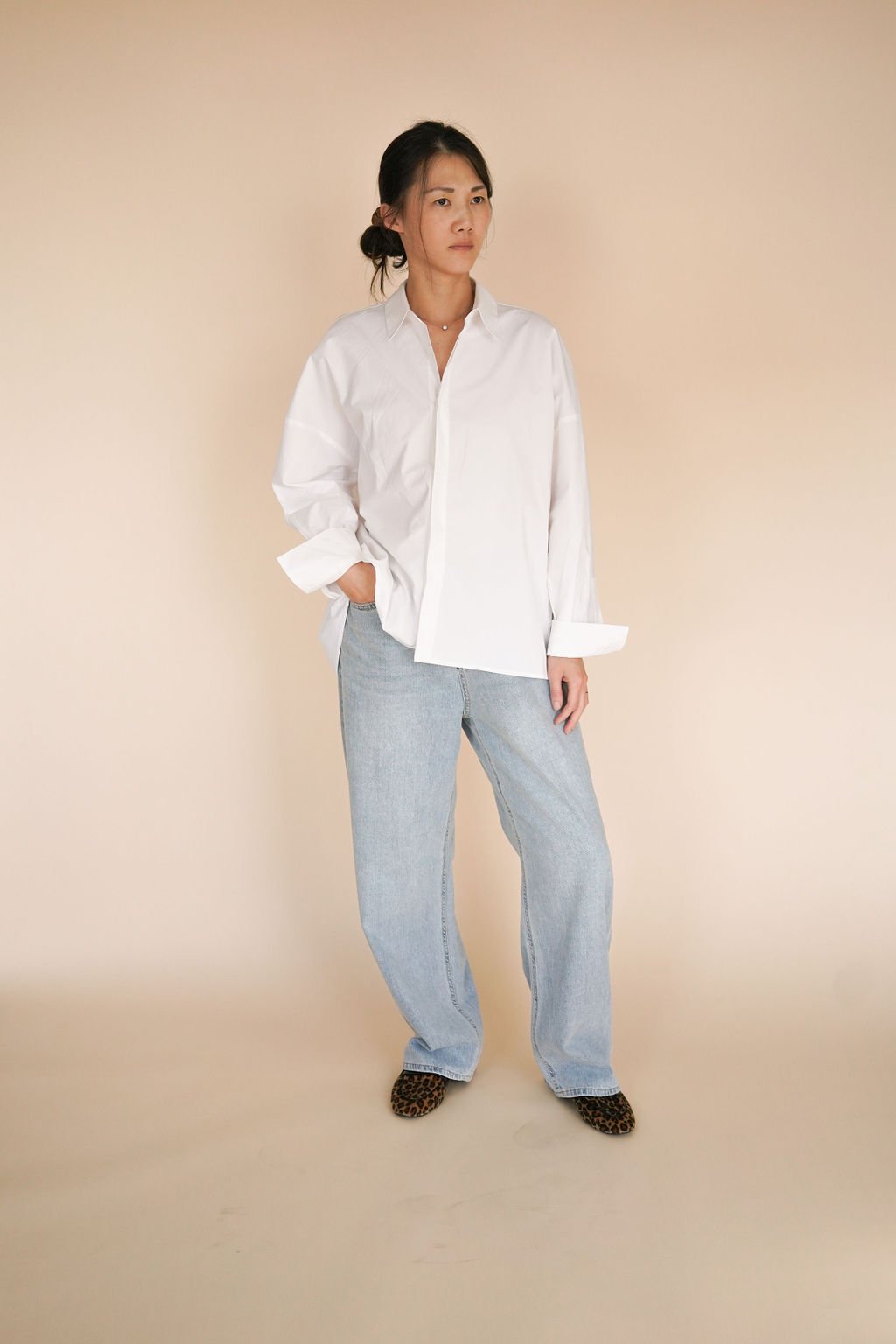 White asymmetrical hem long sleeve poplin shirt made from crisp cotton, featuring a classic collar, concealed button closure, and boxy relaxed fit