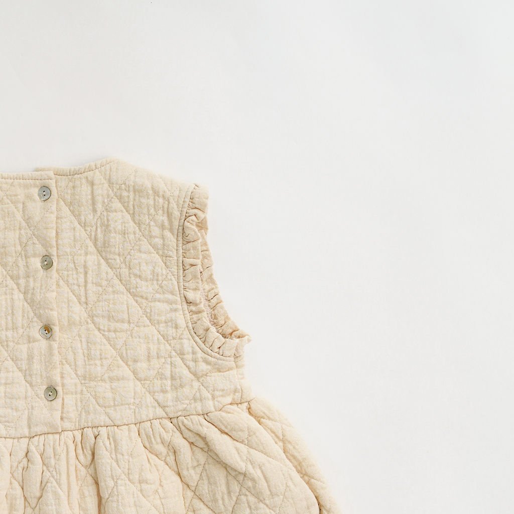 Back Close-up of the quilted pattern and ruffle trim detailing on the kids' ivory dress, highlighting the soft 100% cotton fabric and precise craftsmanship