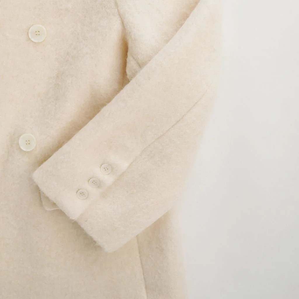 Close-up of Ivory wool-blend coat showing double button closure and soft-textured wool-polyester fabric for a cozy finish