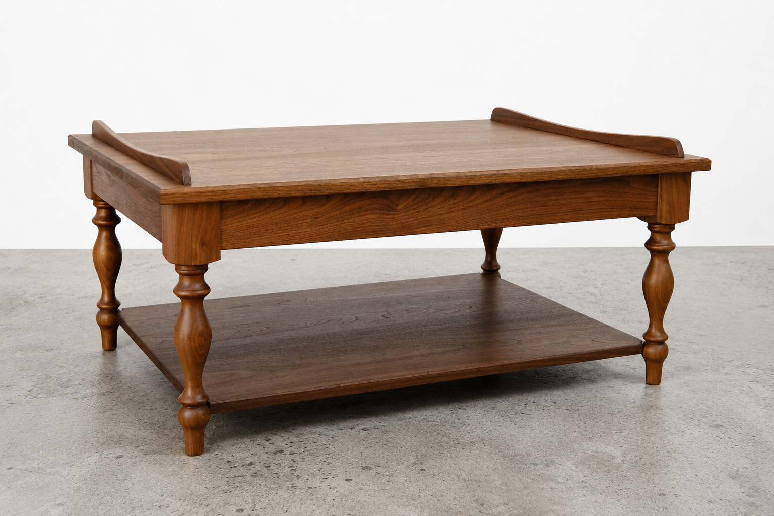 A wooden coffee table with a lower shelf, turned legs, and a raised edge on two sides of the top, set against a plain white wall and on a concrete floor.