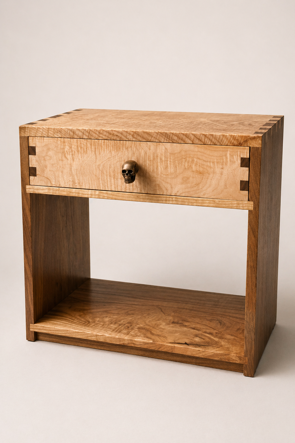 A wooden bedside table with a single drawer featuring a skull-shaped knob, and a large open shelf below.