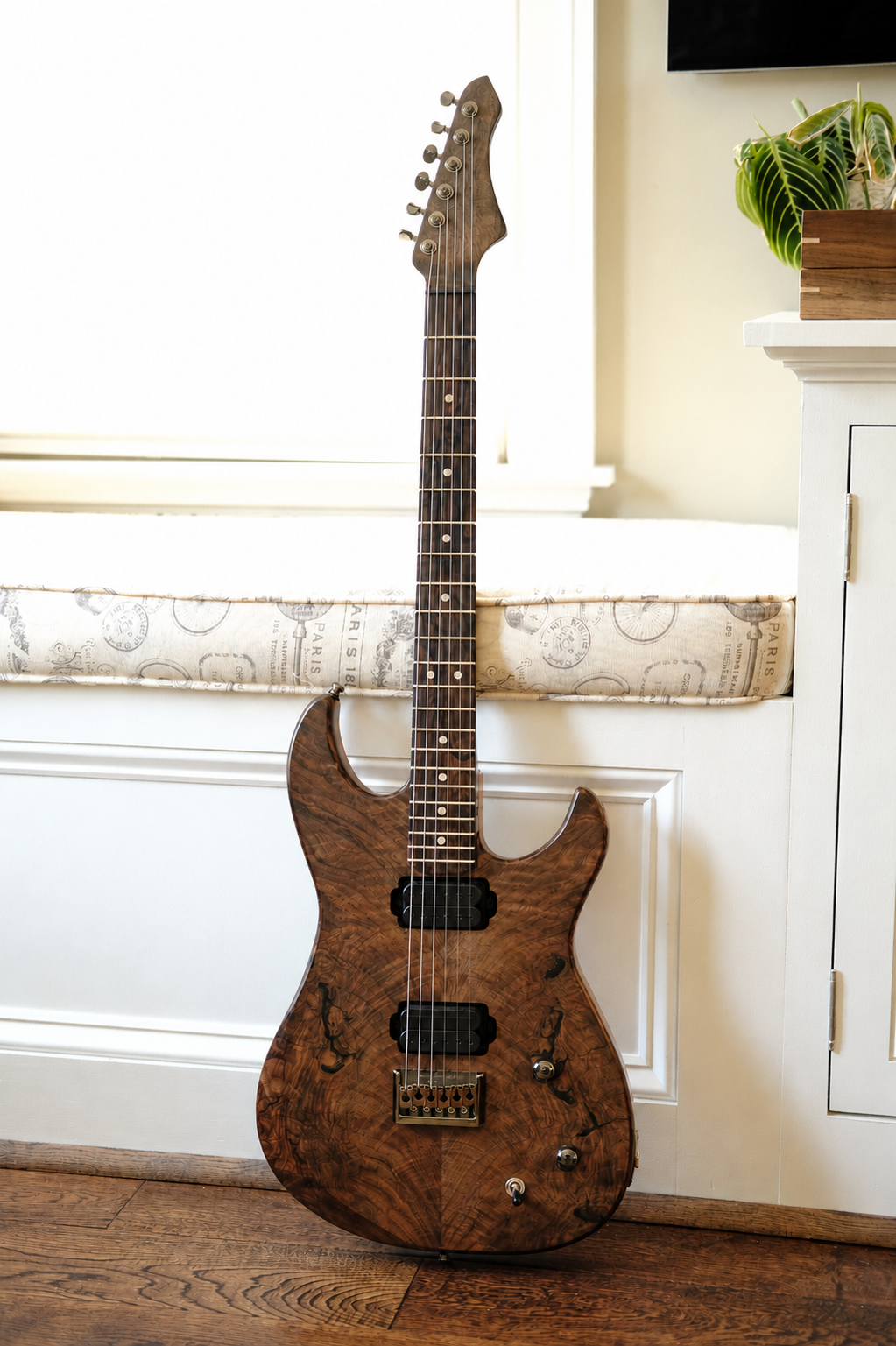 A brown electric guitar with a wood grain finish leaning against a white cabinet in a room with wooden flooring.