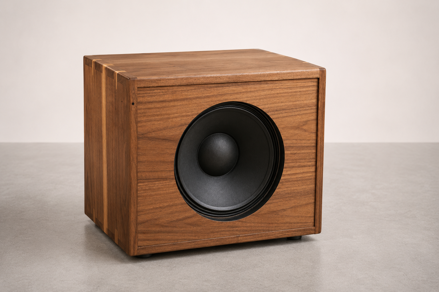 A wooden subwoofer speaker with a large black speaker cone, placed on a gray surface against a plain off-white background.